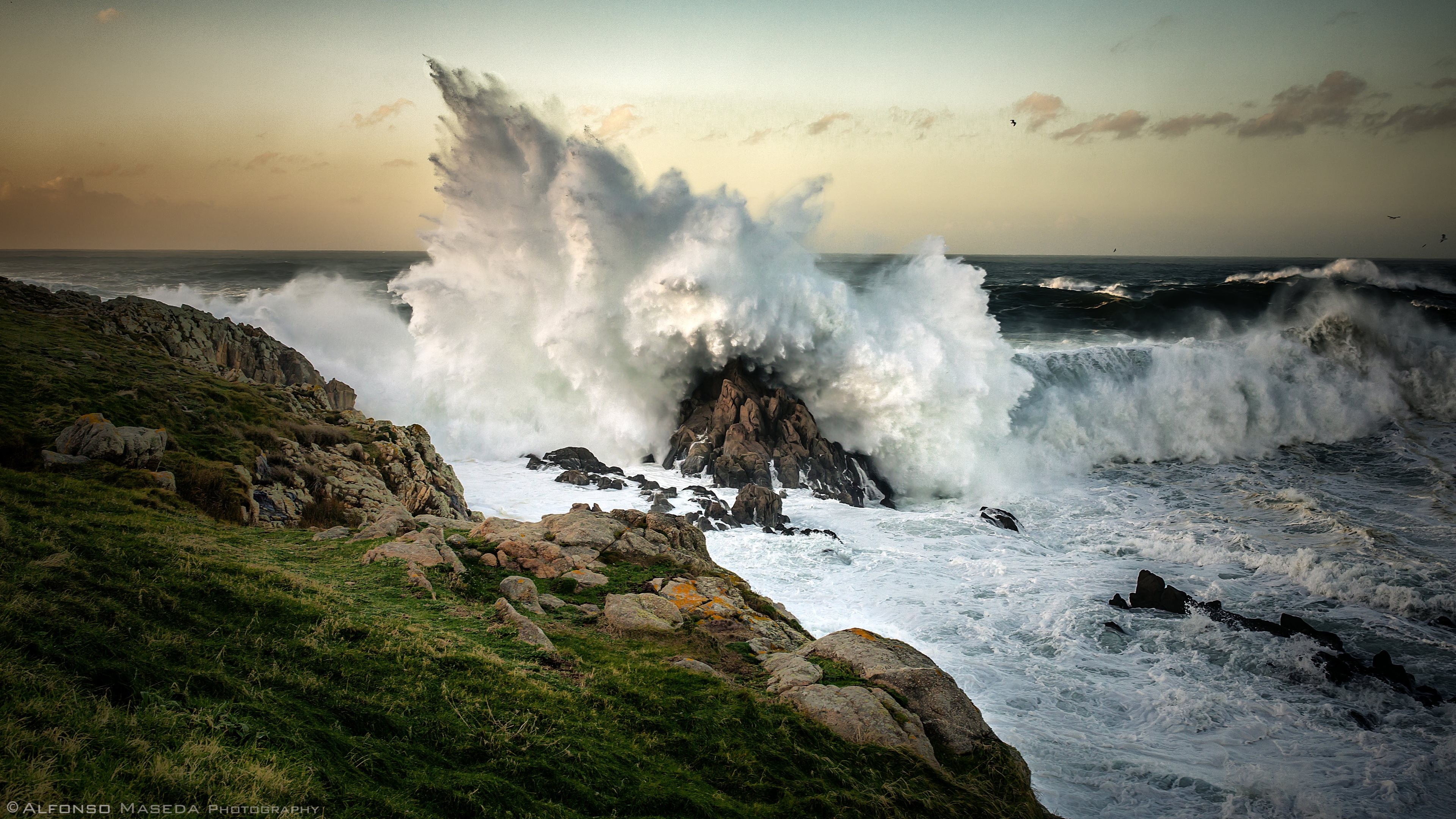 Massive waves crash against rocky shore at sunset HD Wallpaper