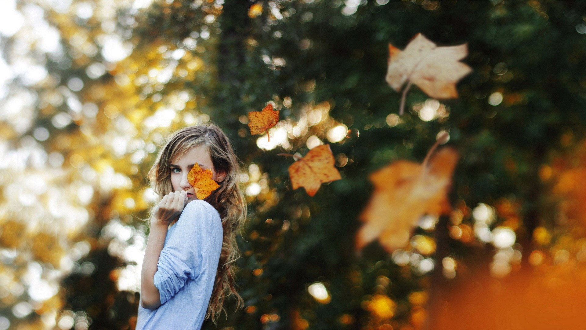 Woman with leaf covering eye in autumn forest HD Wallpaper