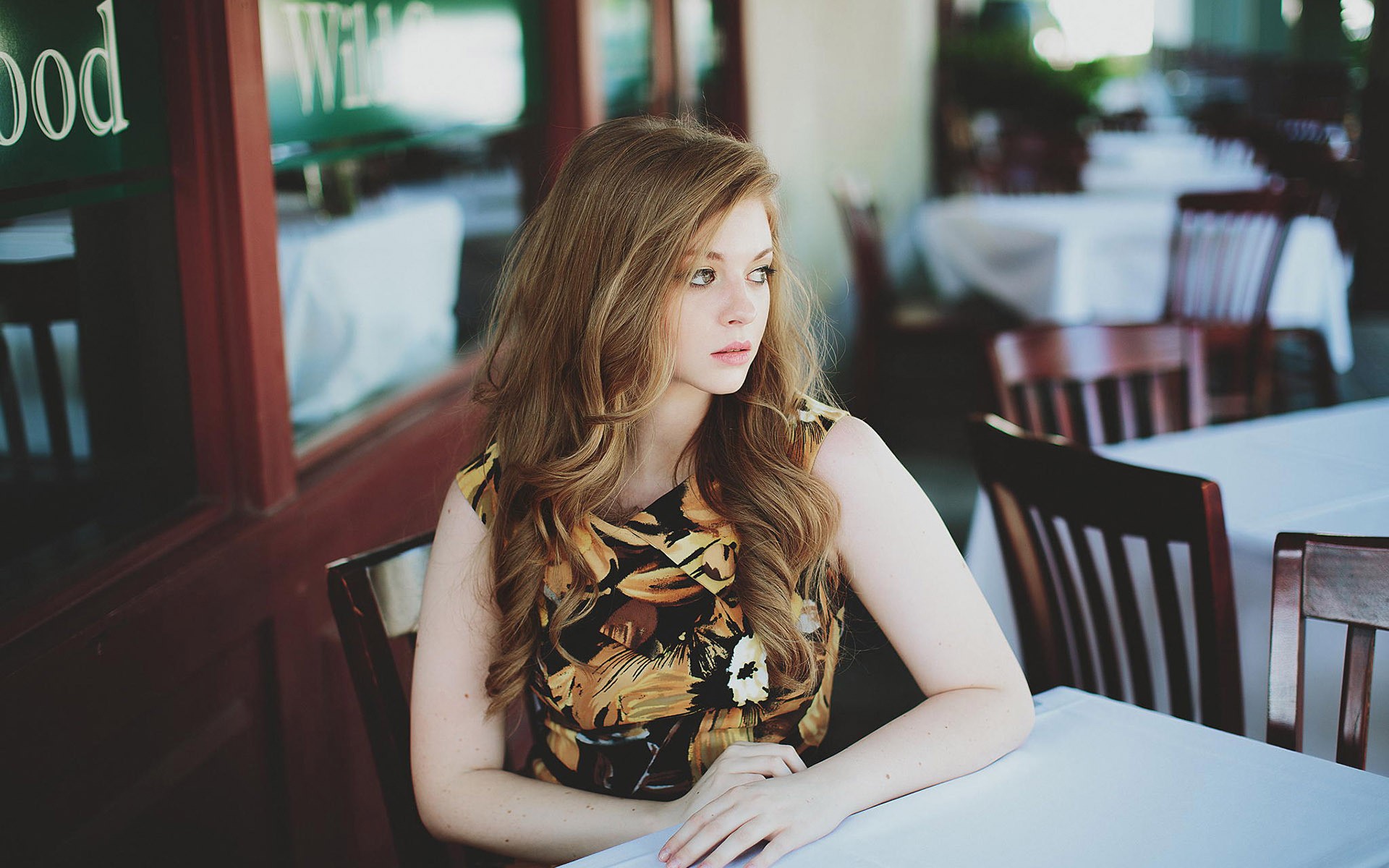 Woman with long auburn hair sitting at a table HD Wallpaper