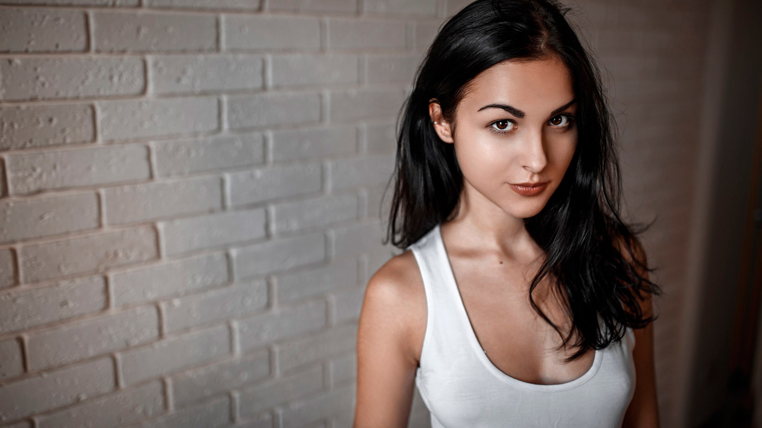 Portrait of a woman in a white tank top against a brick wall HD Wallpaper