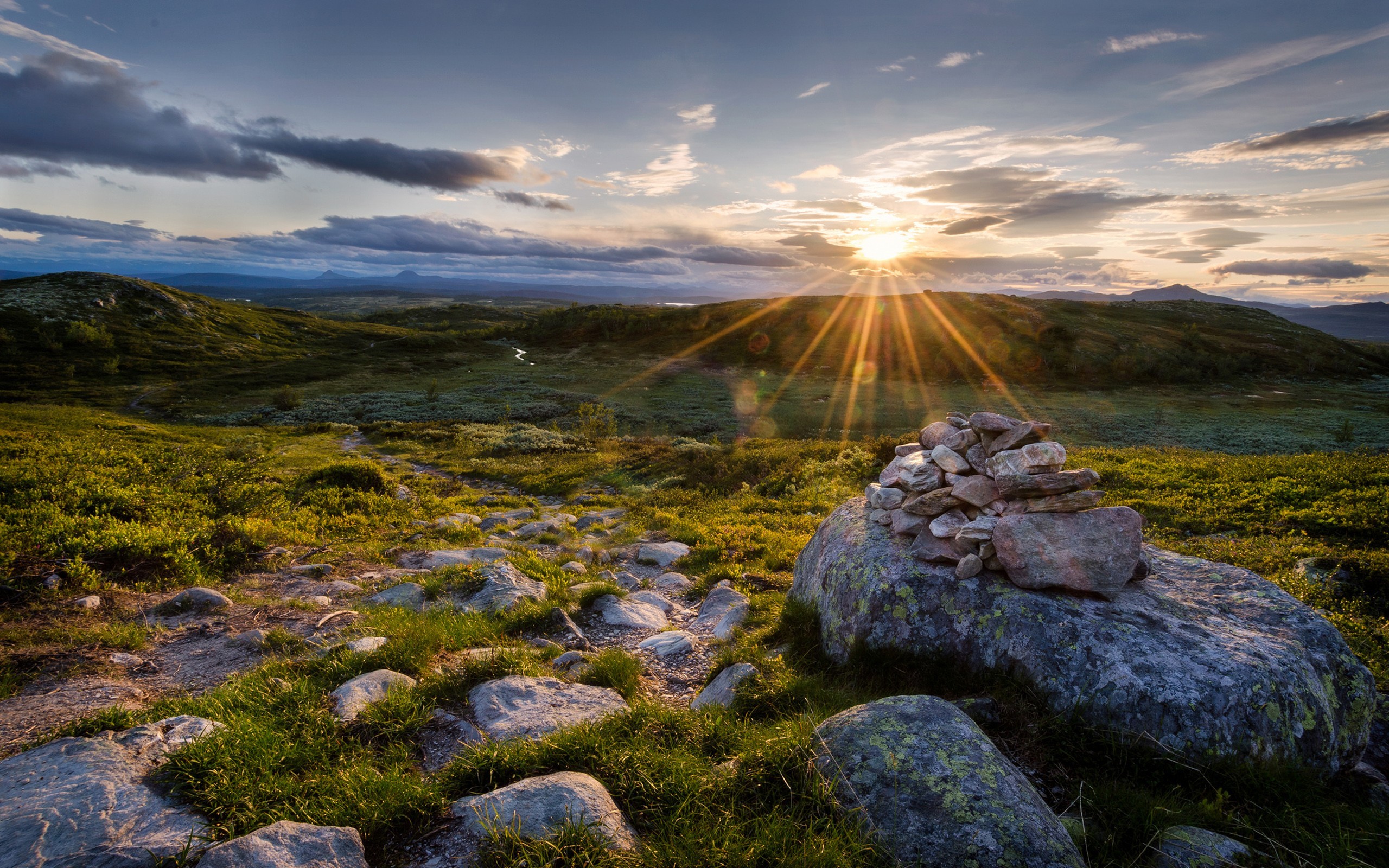 Sun setting over a rocky, grassy landscape HD Wallpaper