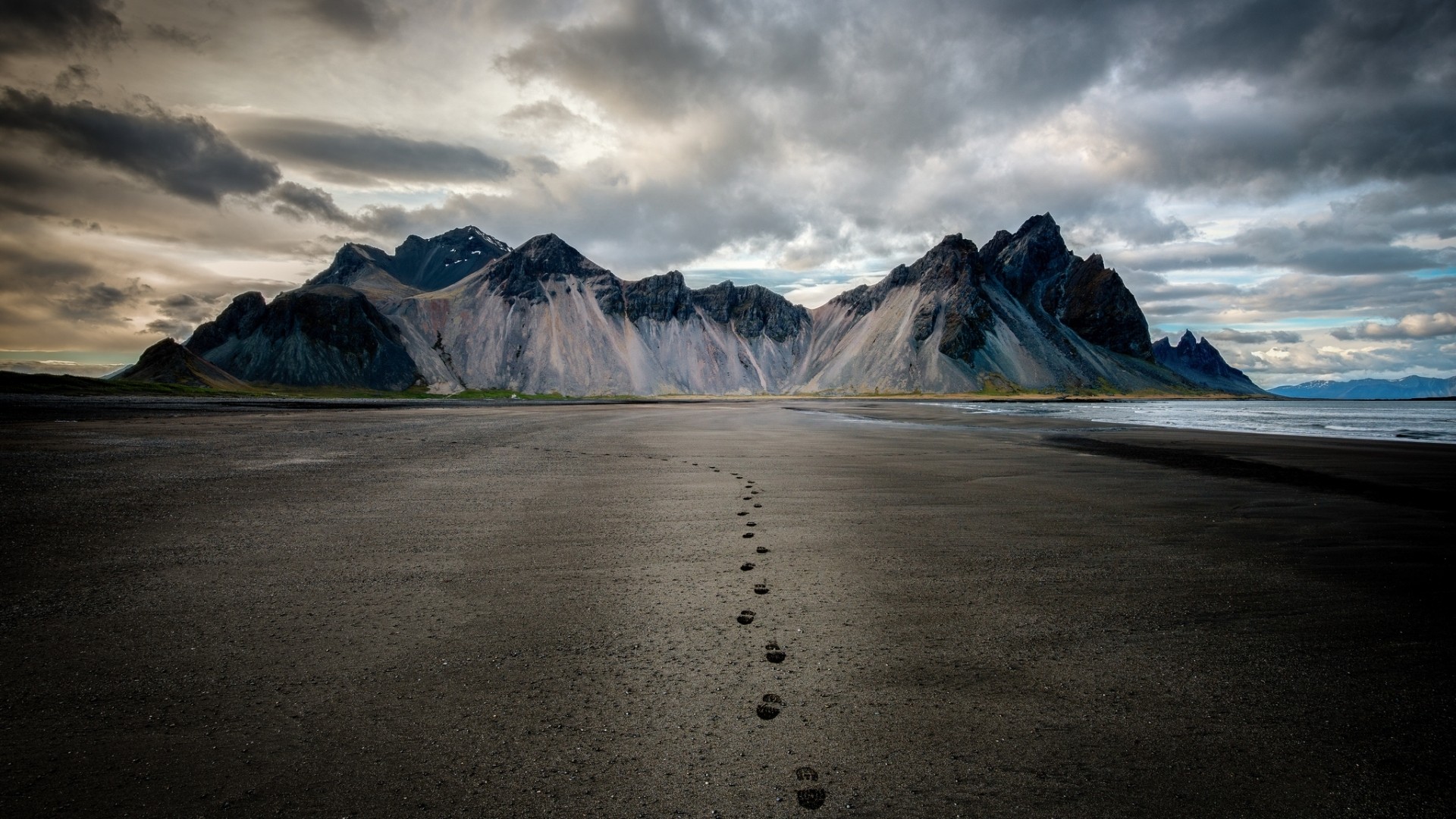 Footprints on a black sand beach leading to mountains in Iceland HD Wallpaper