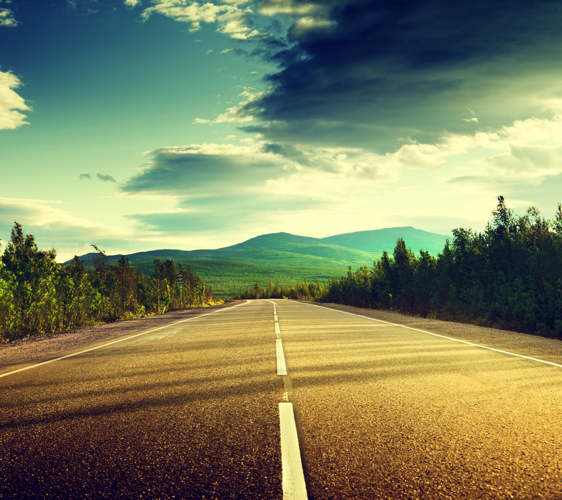 Open road through a green landscape with mountains HD Wallpaper
