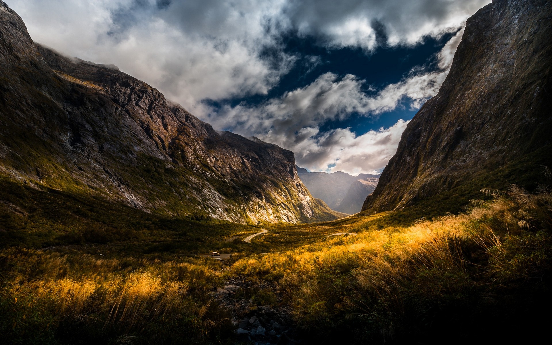 Sunlight illuminates a mountain valley with a winding road HD Wallpaper