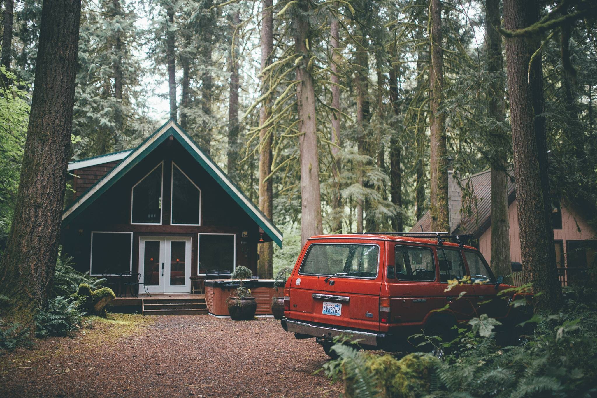 Red SUV parked near a cabin in a Washington state forest HD Wallpaper