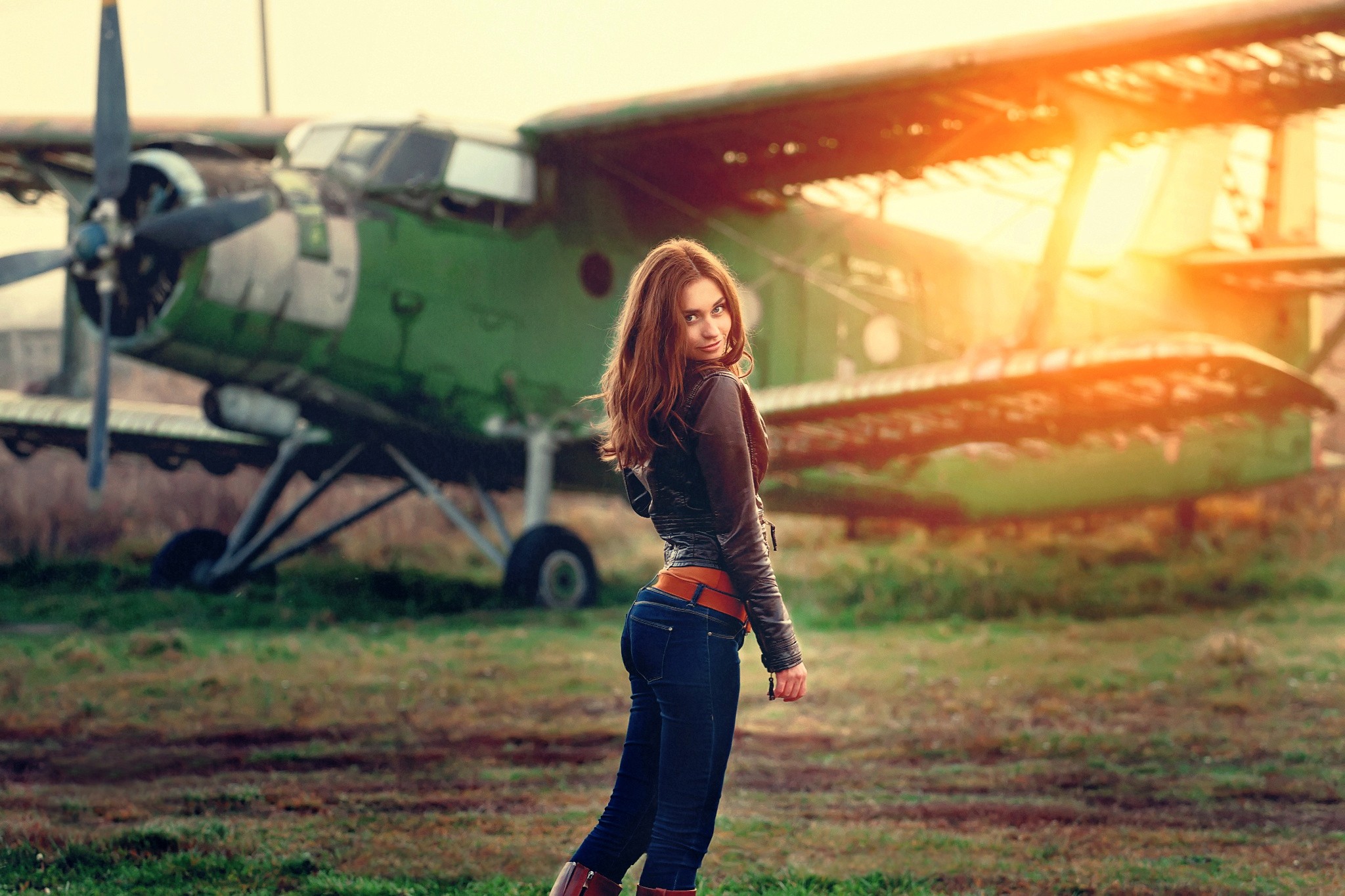Woman in leather jacket and jeans posing near Antonov An-2 aircraft HD Wallpaper