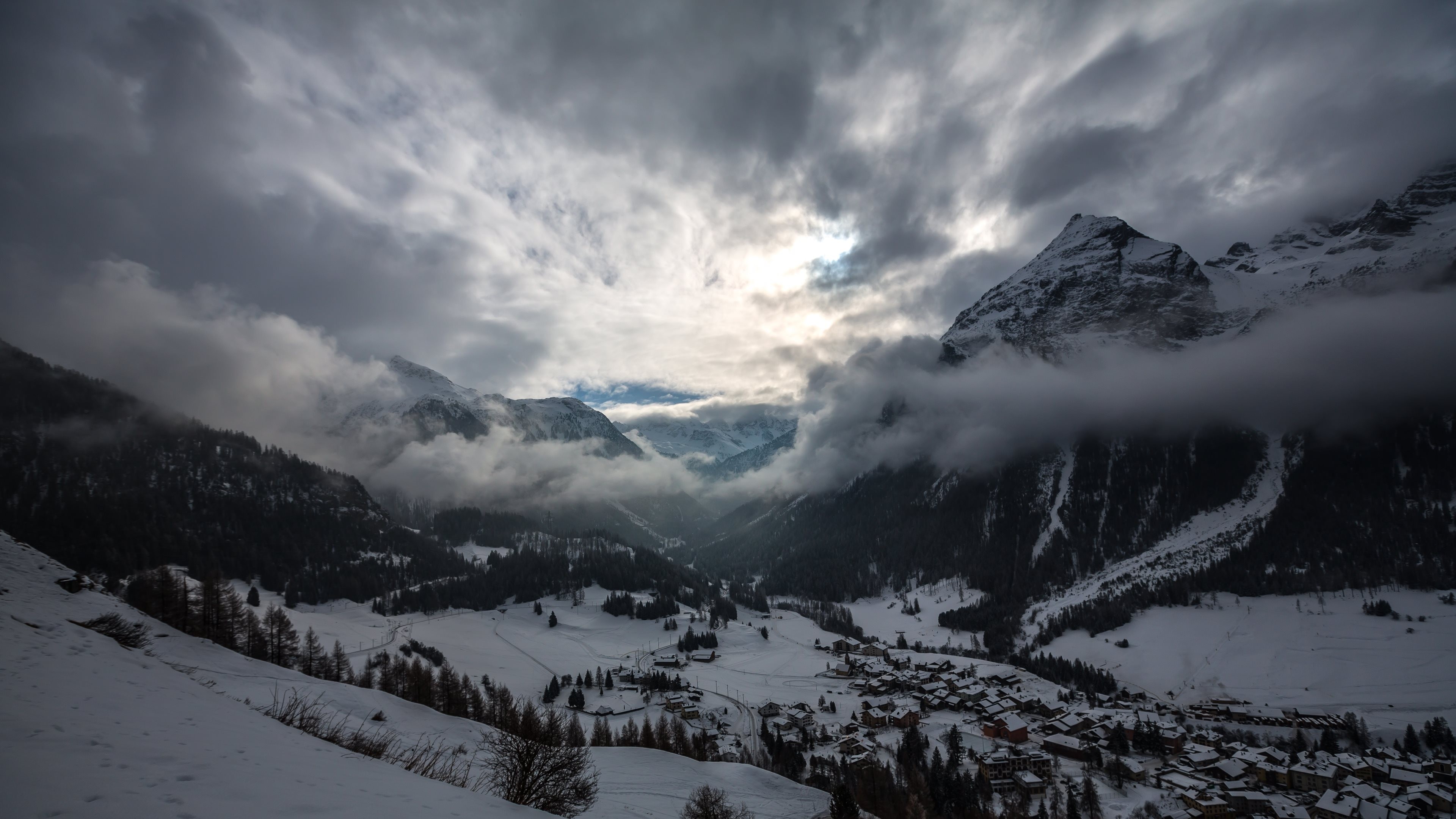 Snowy mountains with clouds and a village HD Wallpaper