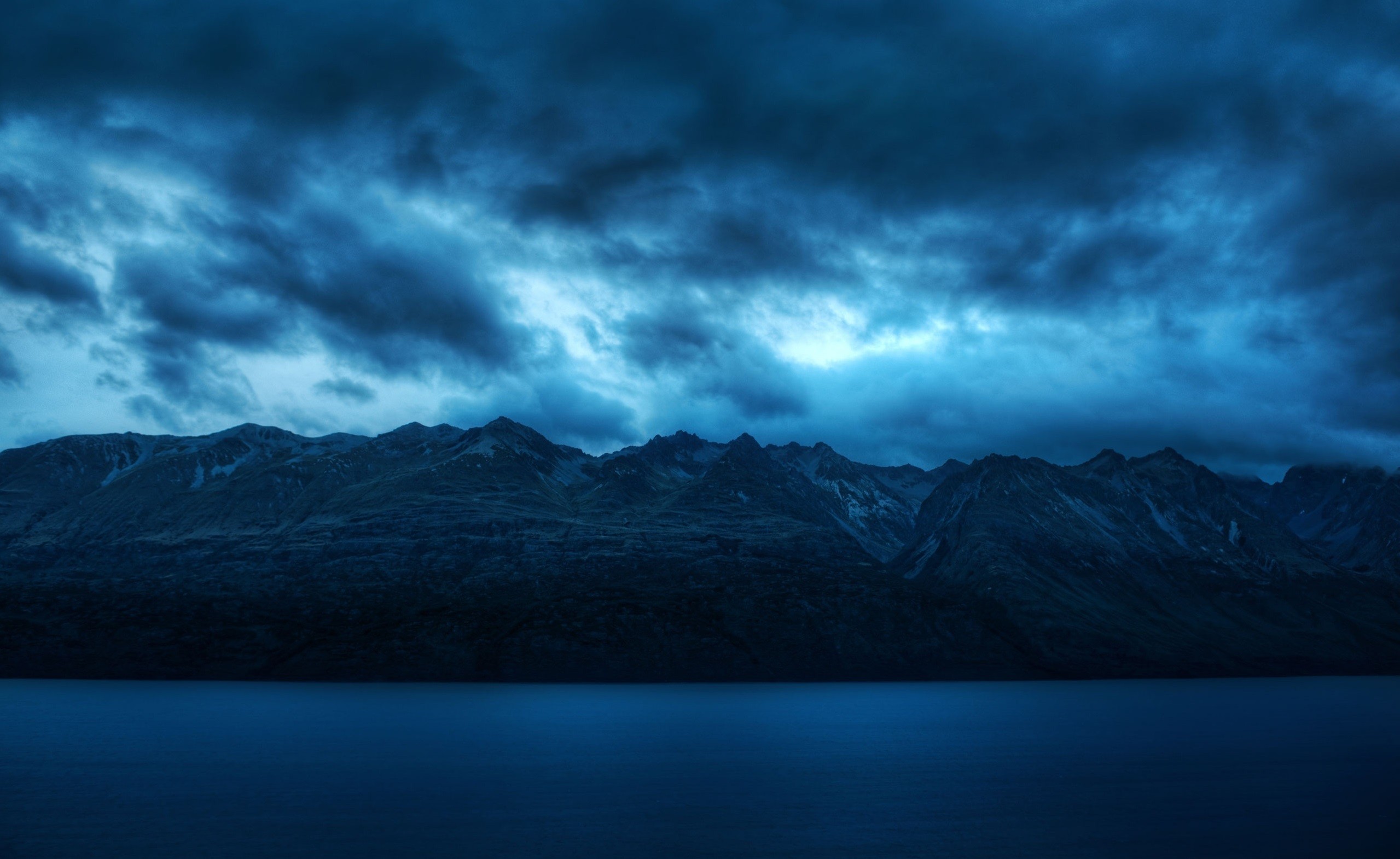Dark clouds over mountains and a lake HD Wallpaper