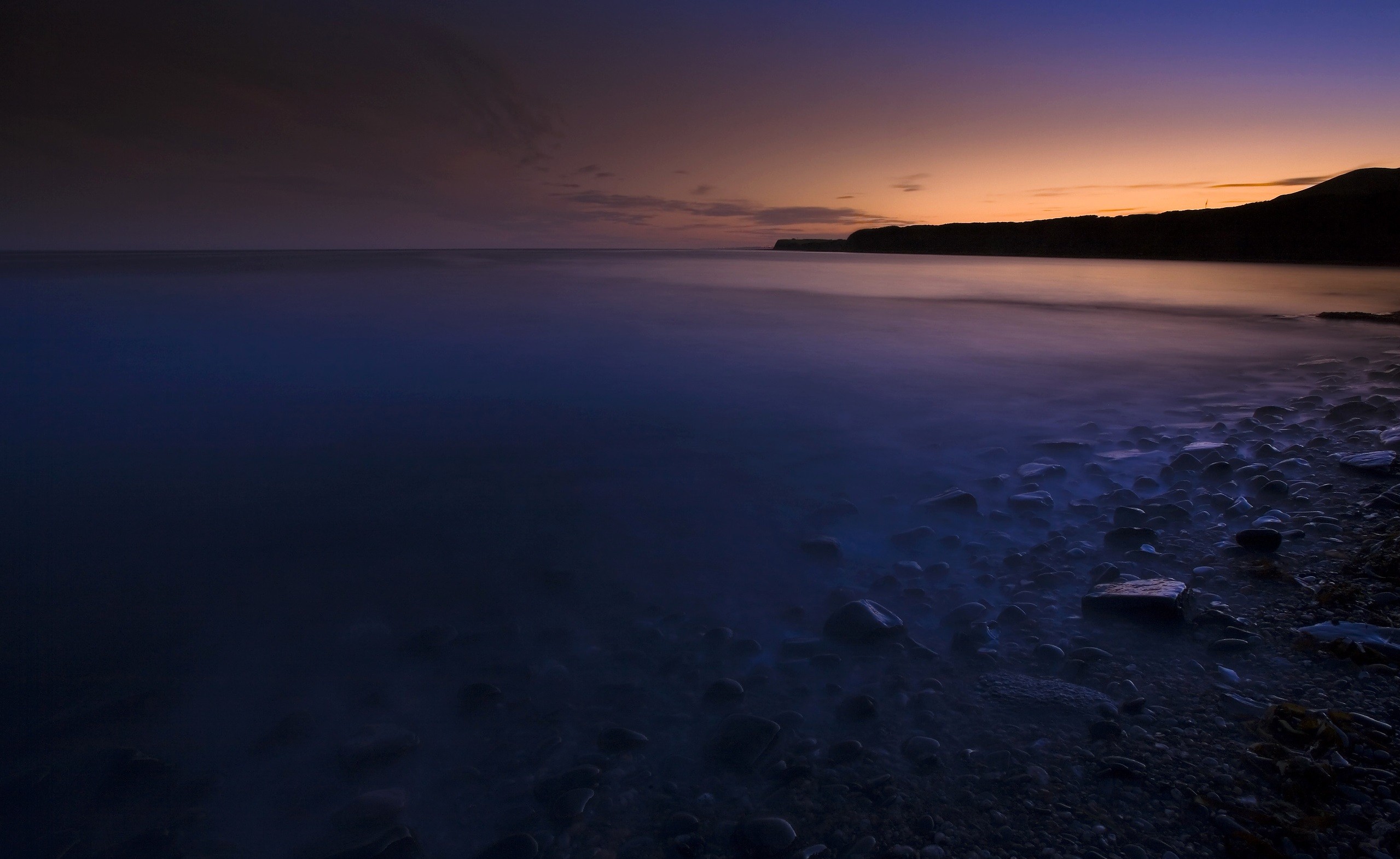 Coastline at dusk with smooth water and stones HD Wallpaper