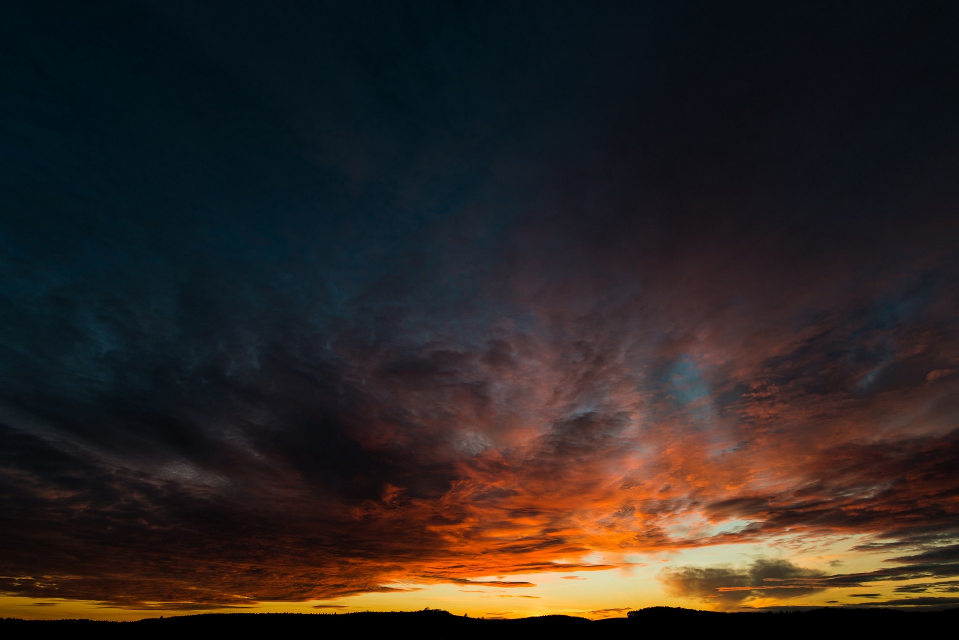 Dramatic sunset clouds over a silhouetted landscape HD Wallpaper