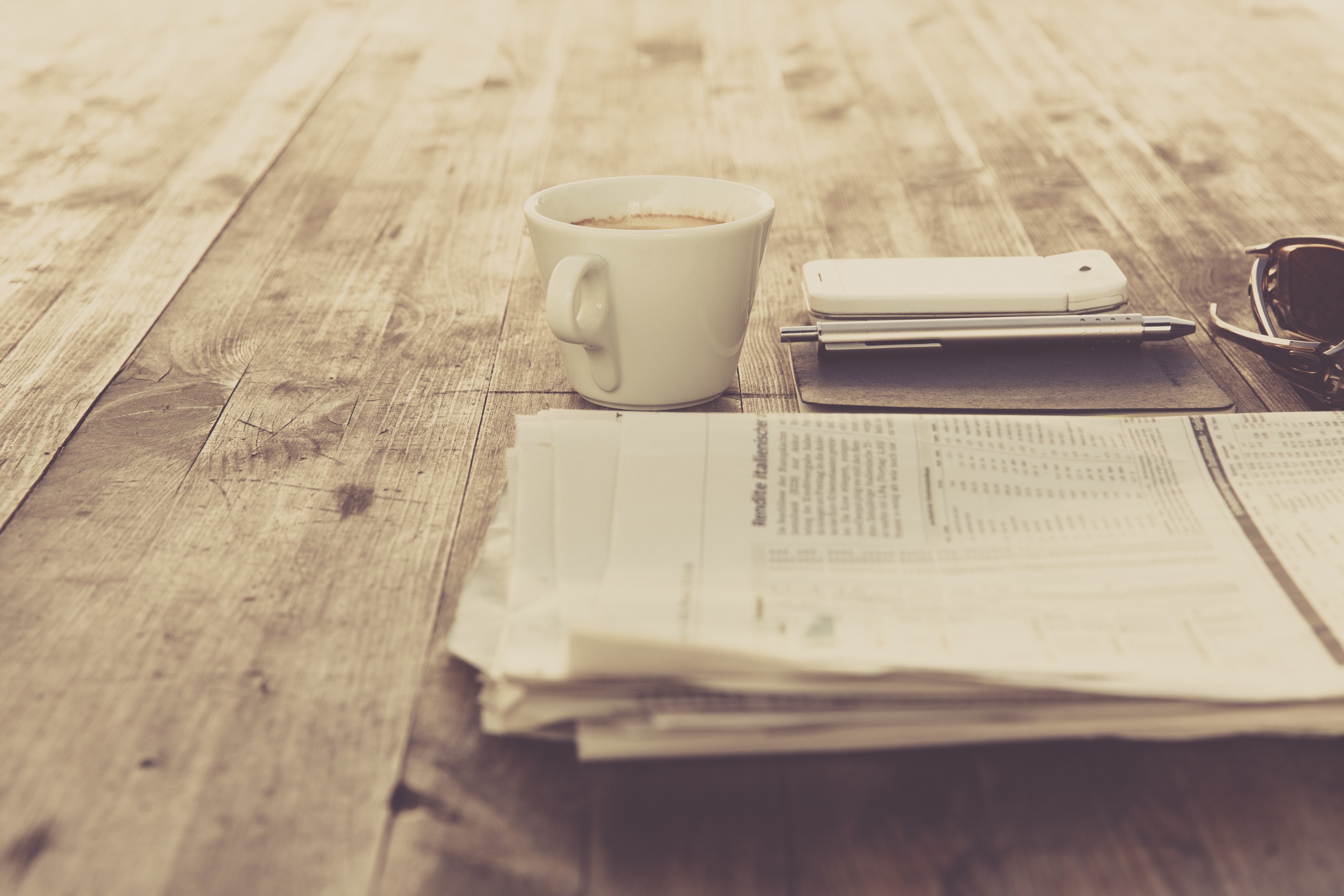 Coffee cup, smartphone, pen, and newspaper on a wooden table HD Wallpaper
