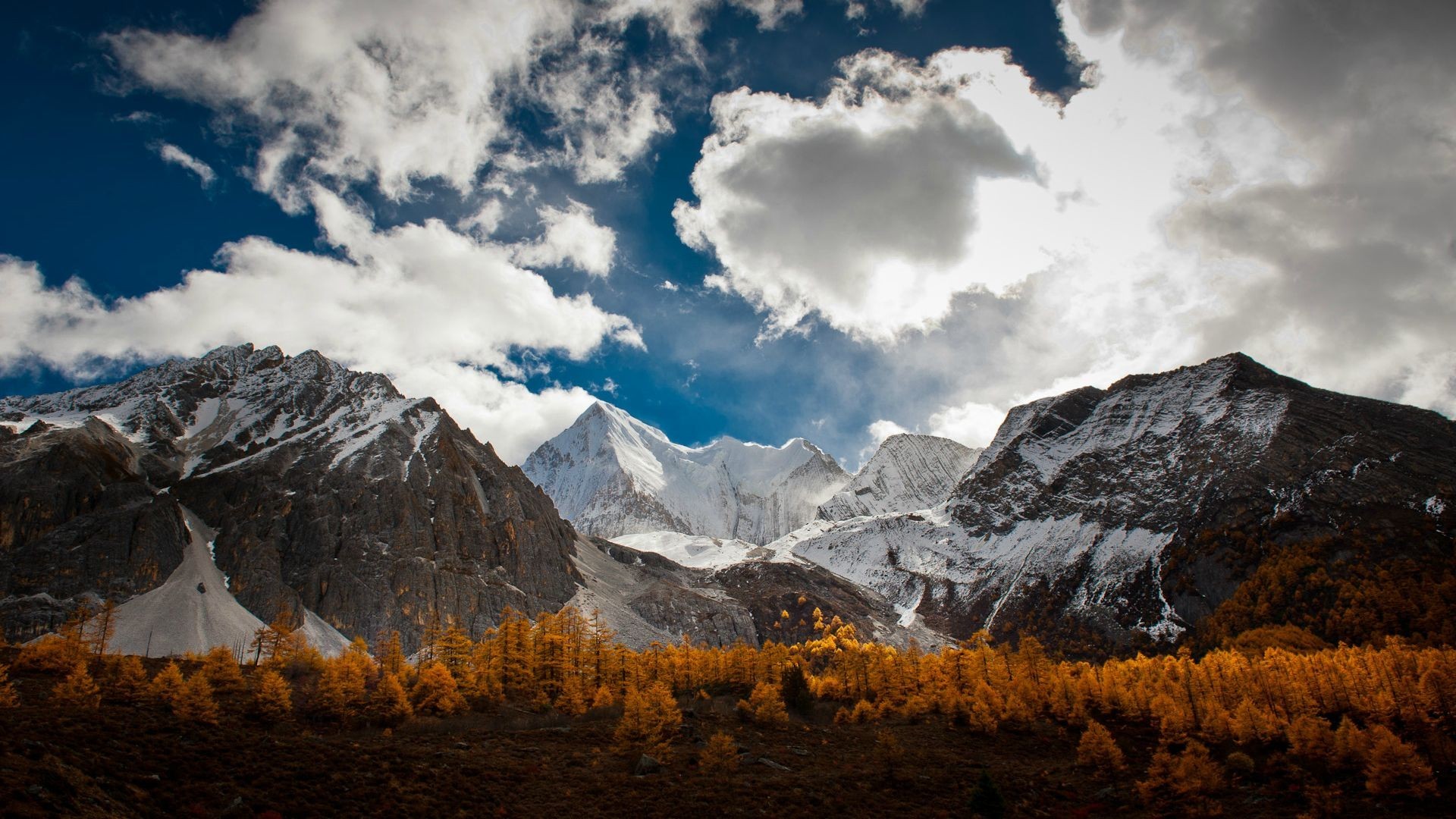 Snow-capped mountains and autumn forest under a cloudy sky HD Wallpaper