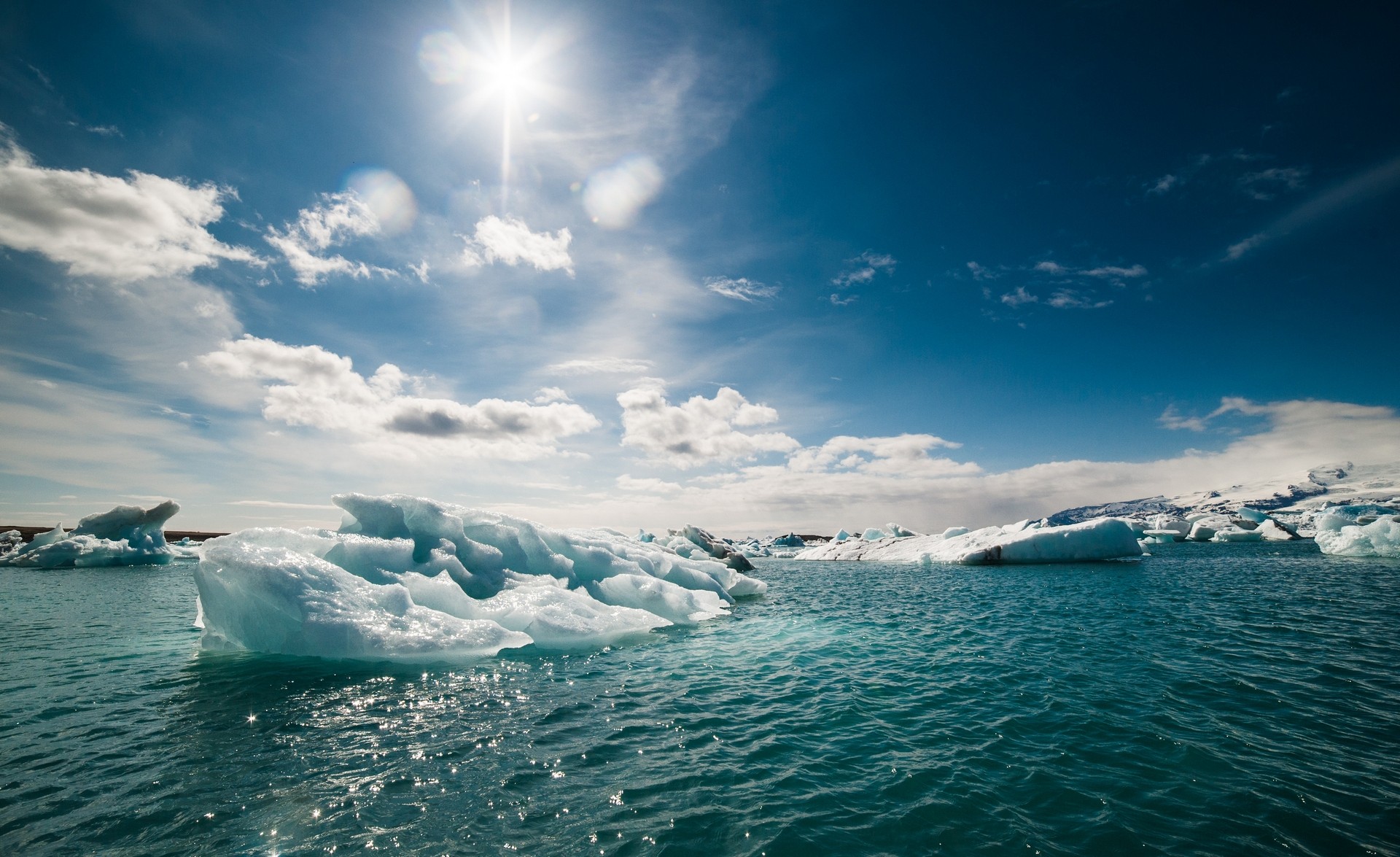 Icebergs floating in turquoise water under a bright sun HD Wallpaper