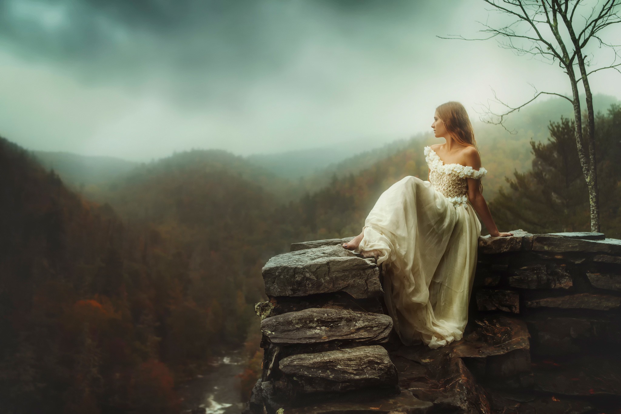 Woman in a white dress sitting on a stone ledge overlooking a misty valley HD Wallpaper