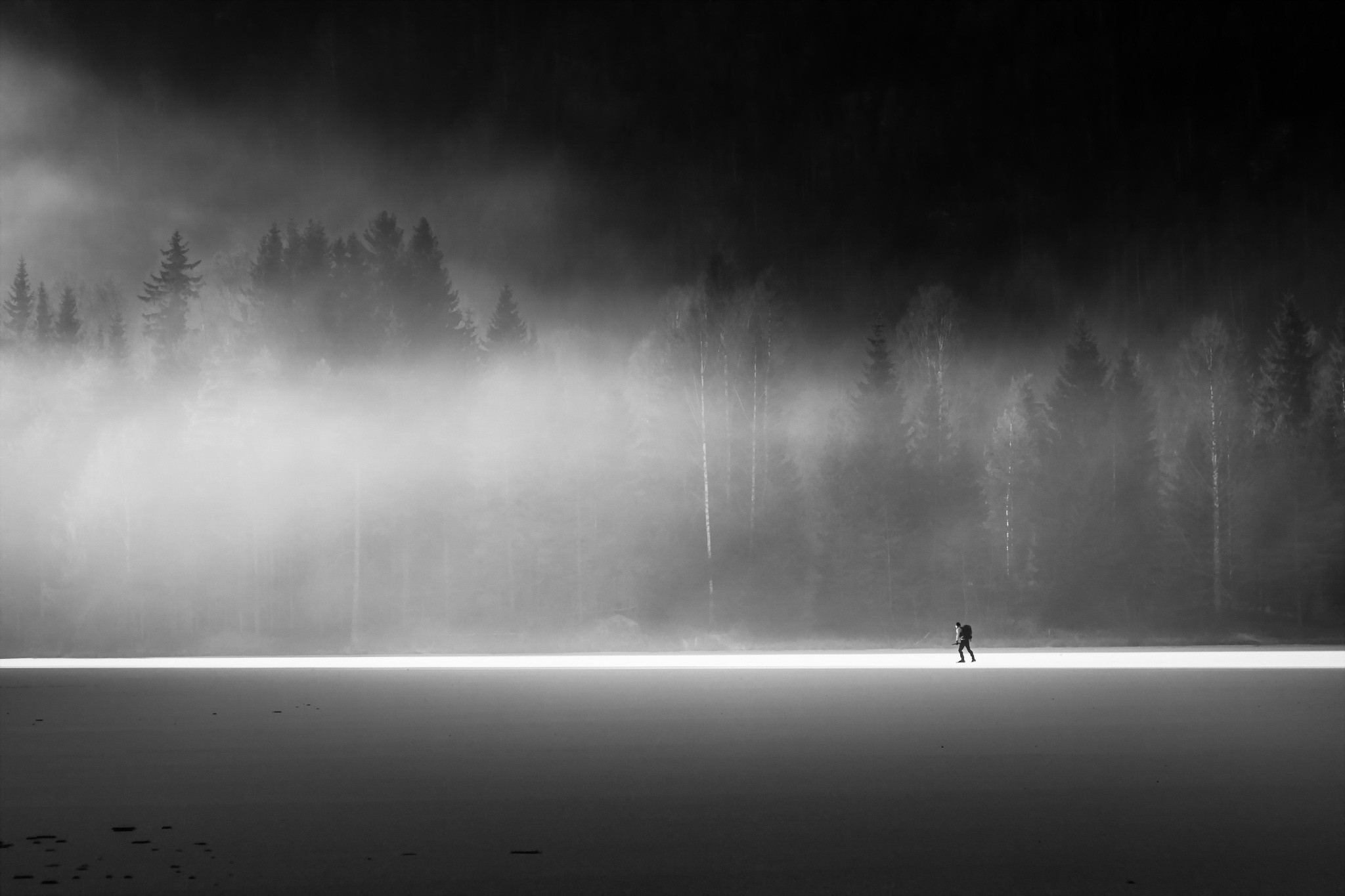 Person walking on a frozen lake with misty forest background HD Wallpaper