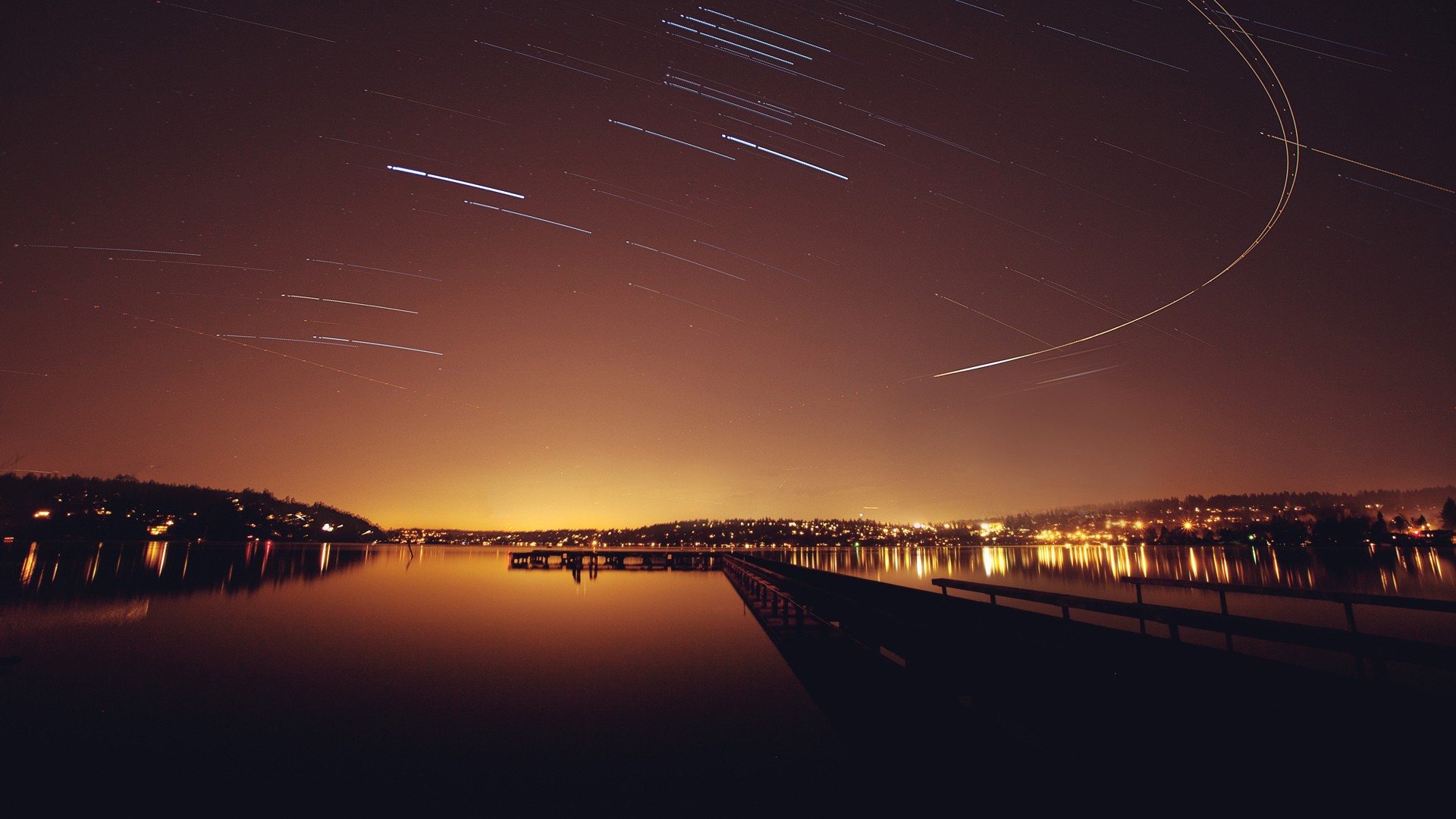 Star trails over a lake and city at night HD Wallpaper