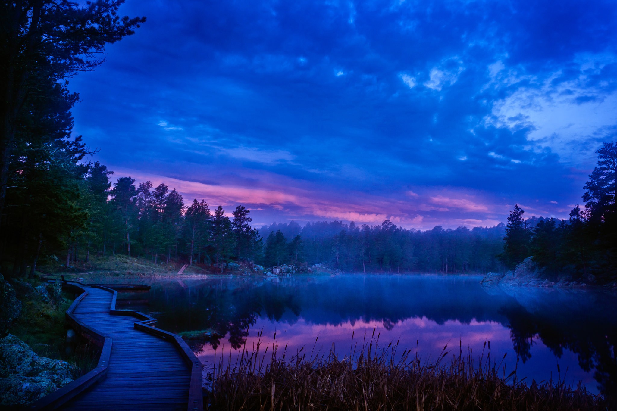 Wooden boardwalk along a misty lake at twilight HD Wallpaper