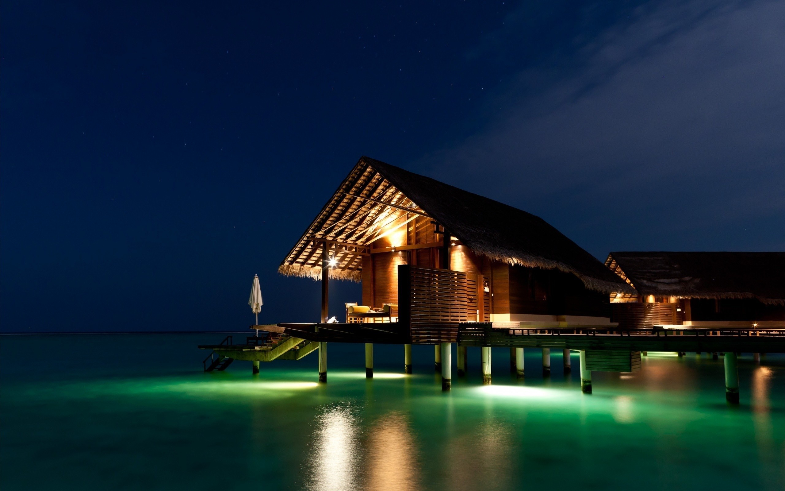 Overwater bungalows at night with glowing water HD Wallpaper