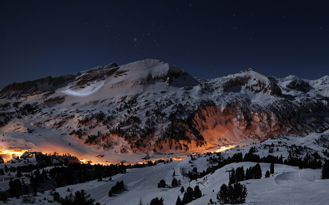 Snowy mountains at night with village lights HD Wallpaper