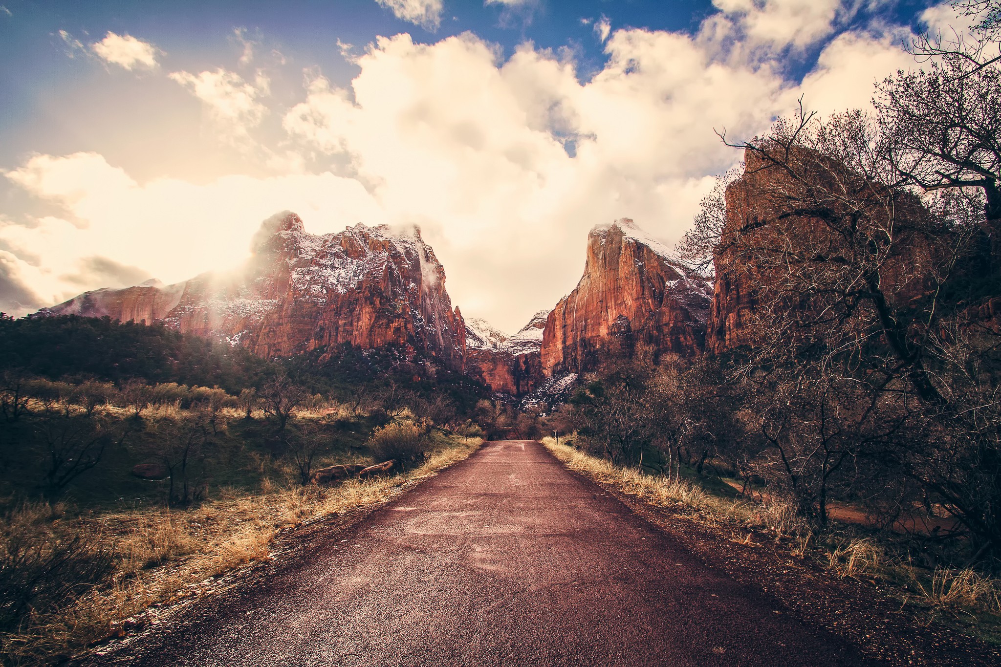 Road leading to snow-capped mountains under a cloudy sky HD Wallpaper