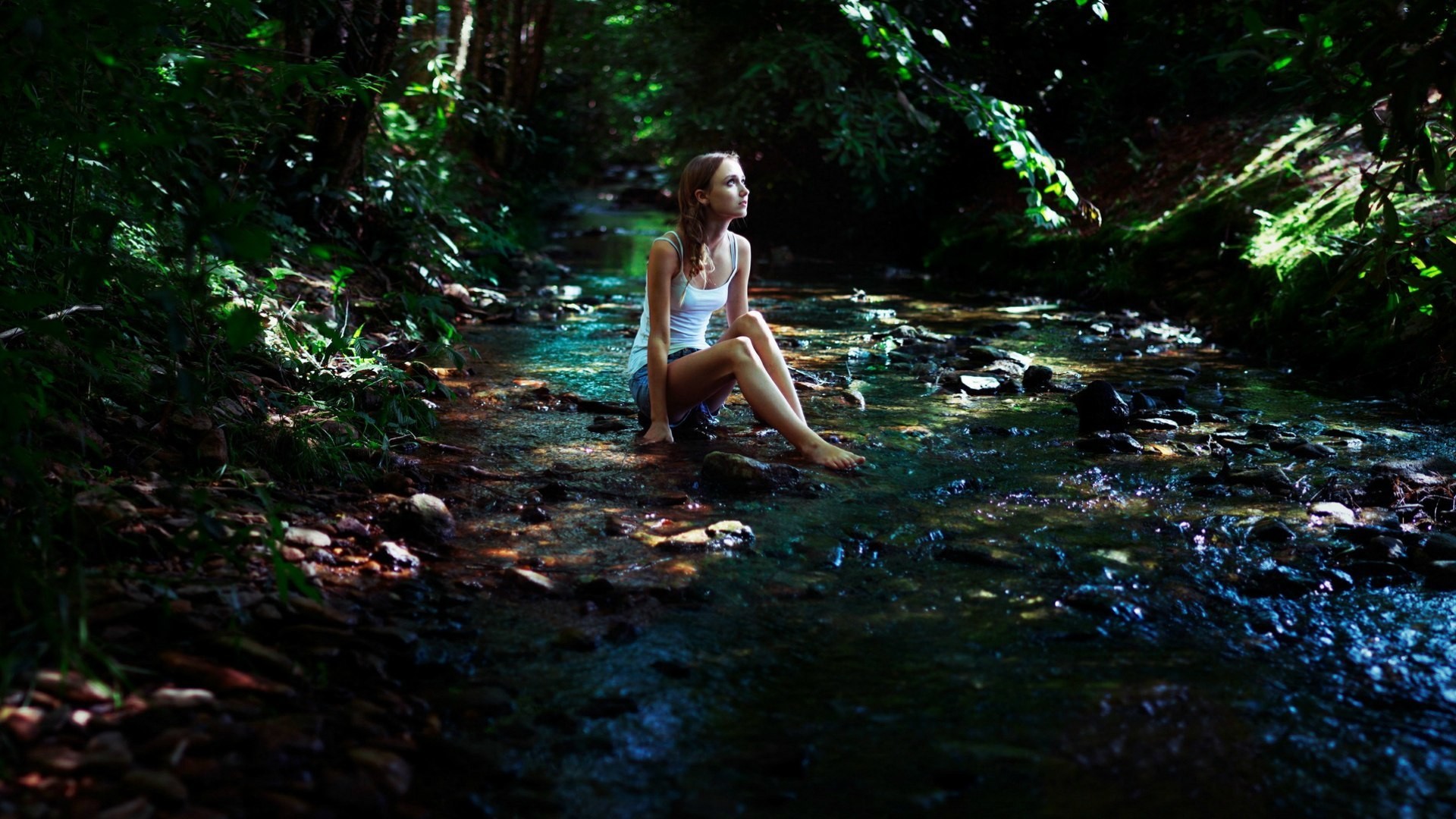 Woman sitting in a stream in a forest HD Wallpaper