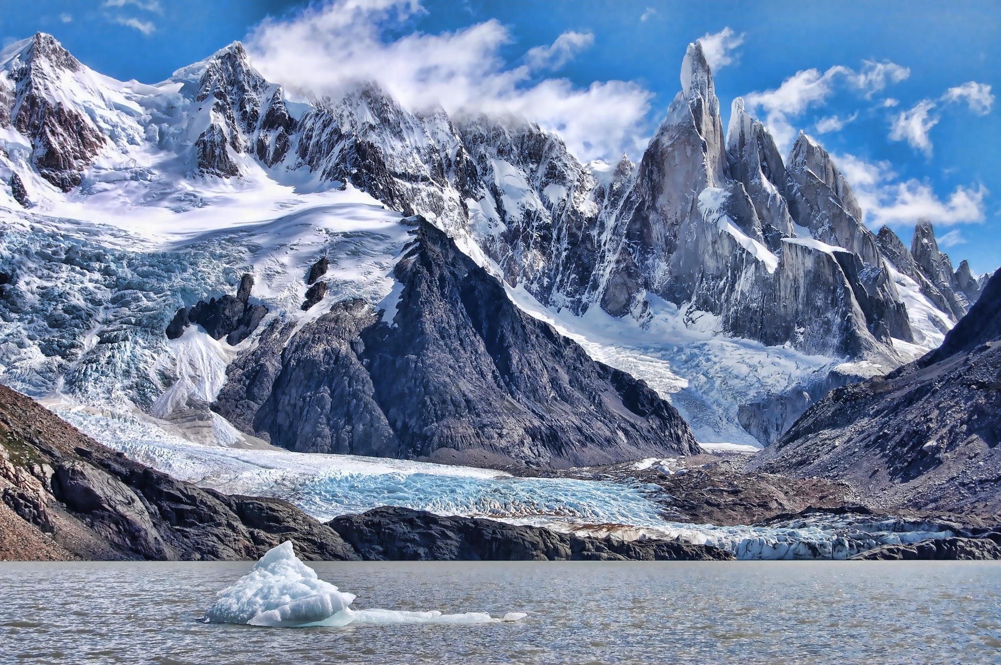 Jagged snow-capped mountains rise above a glacial lake HD Wallpaper