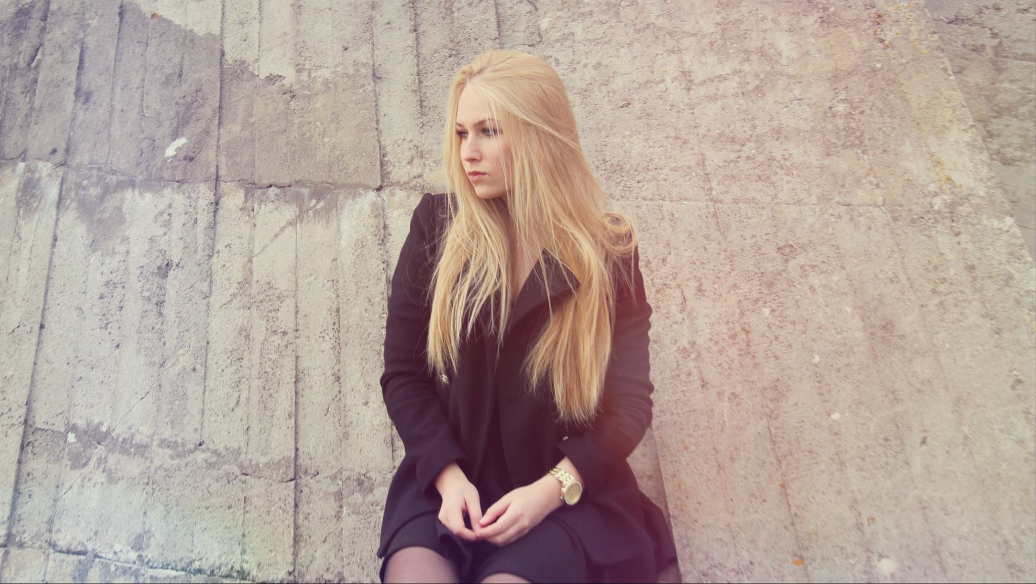 Woman with blonde hair sitting against a concrete wall HD Wallpaper
