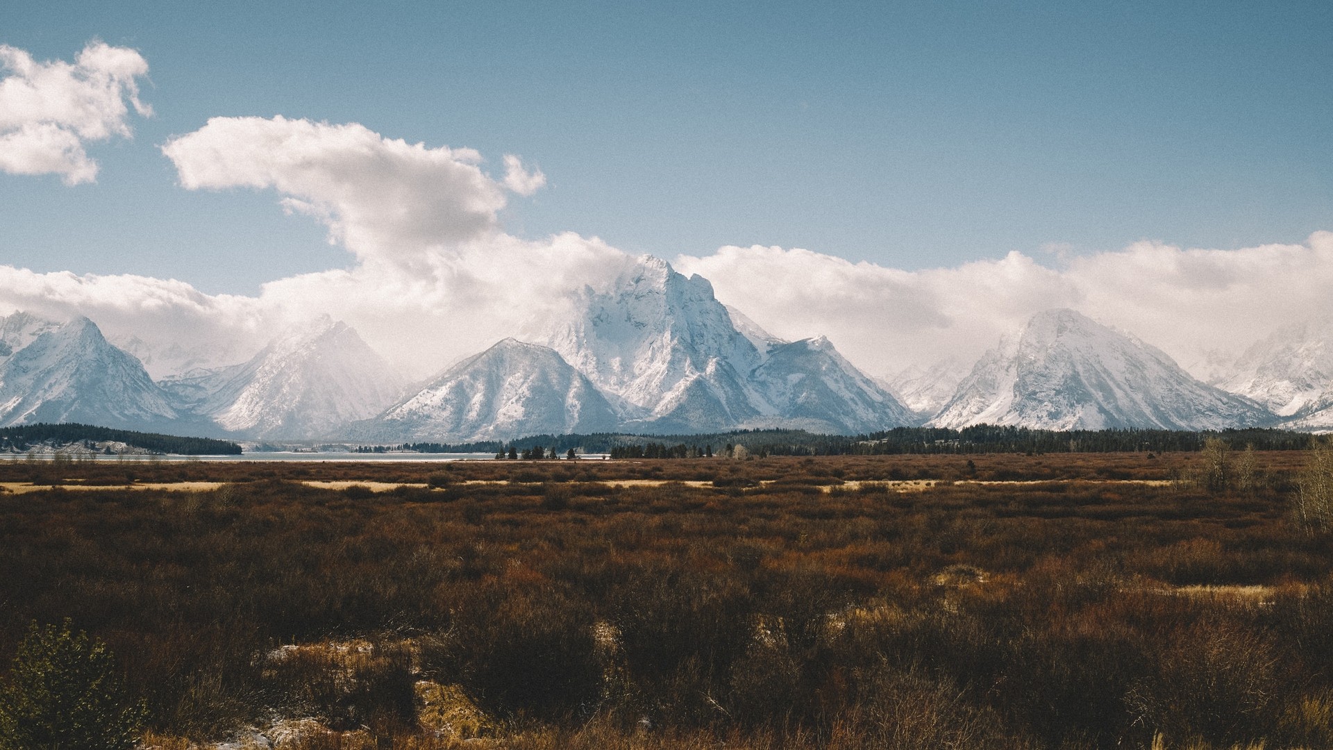 Snow-capped mountains over a field and lake HD Wallpaper