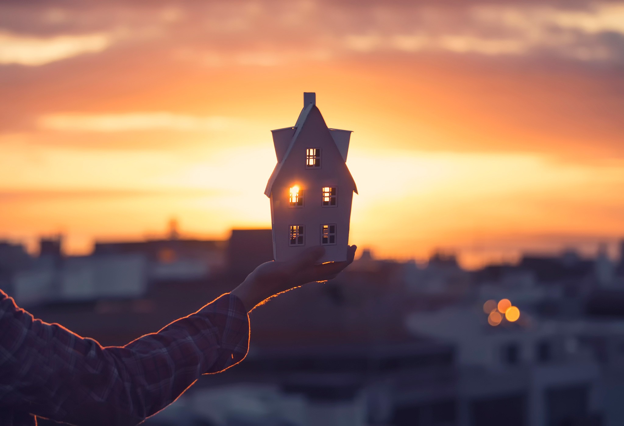 Hand holding a model house at sunset HD Wallpaper