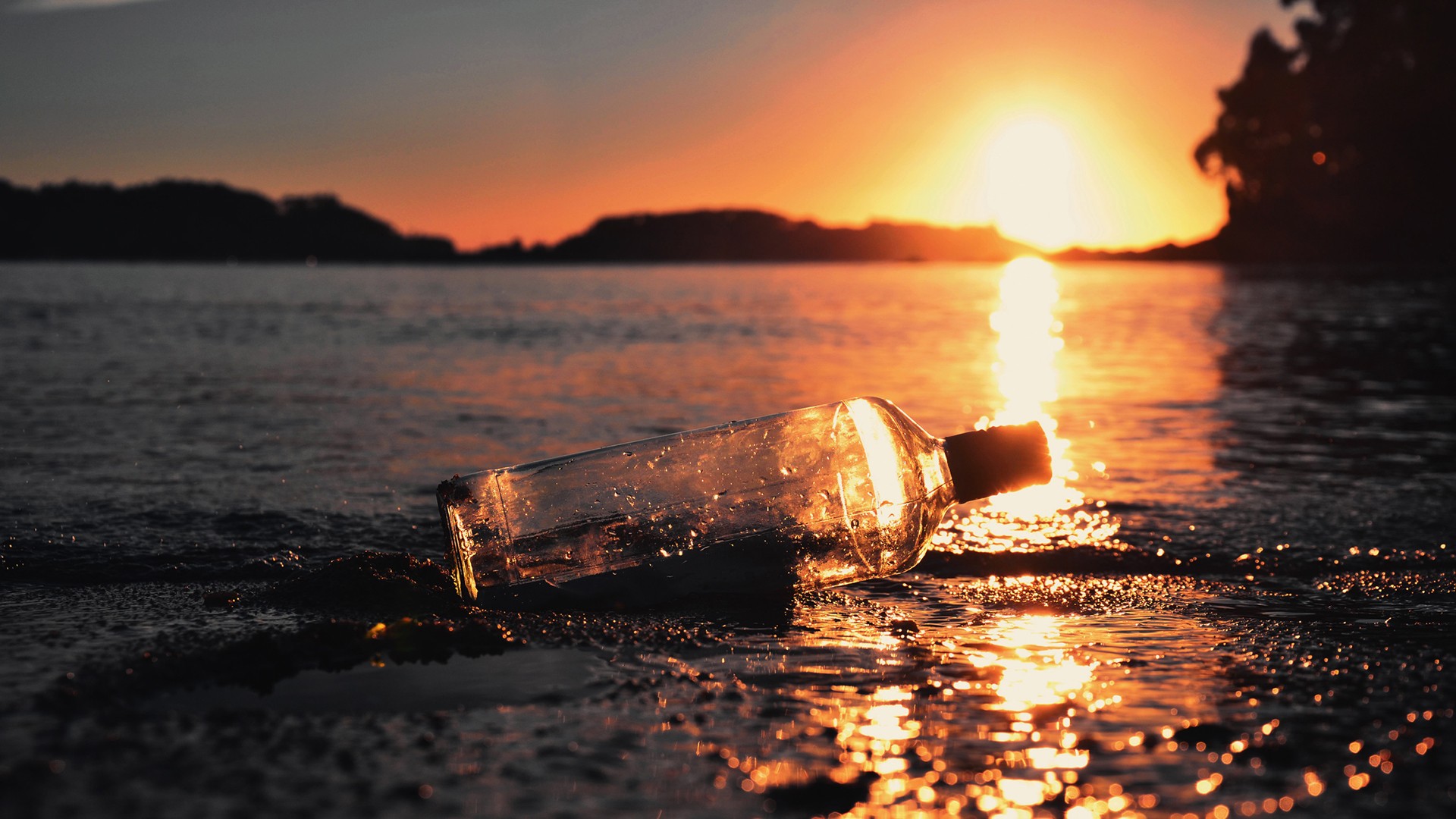 Glass bottle on the shore at sunset HD Wallpaper