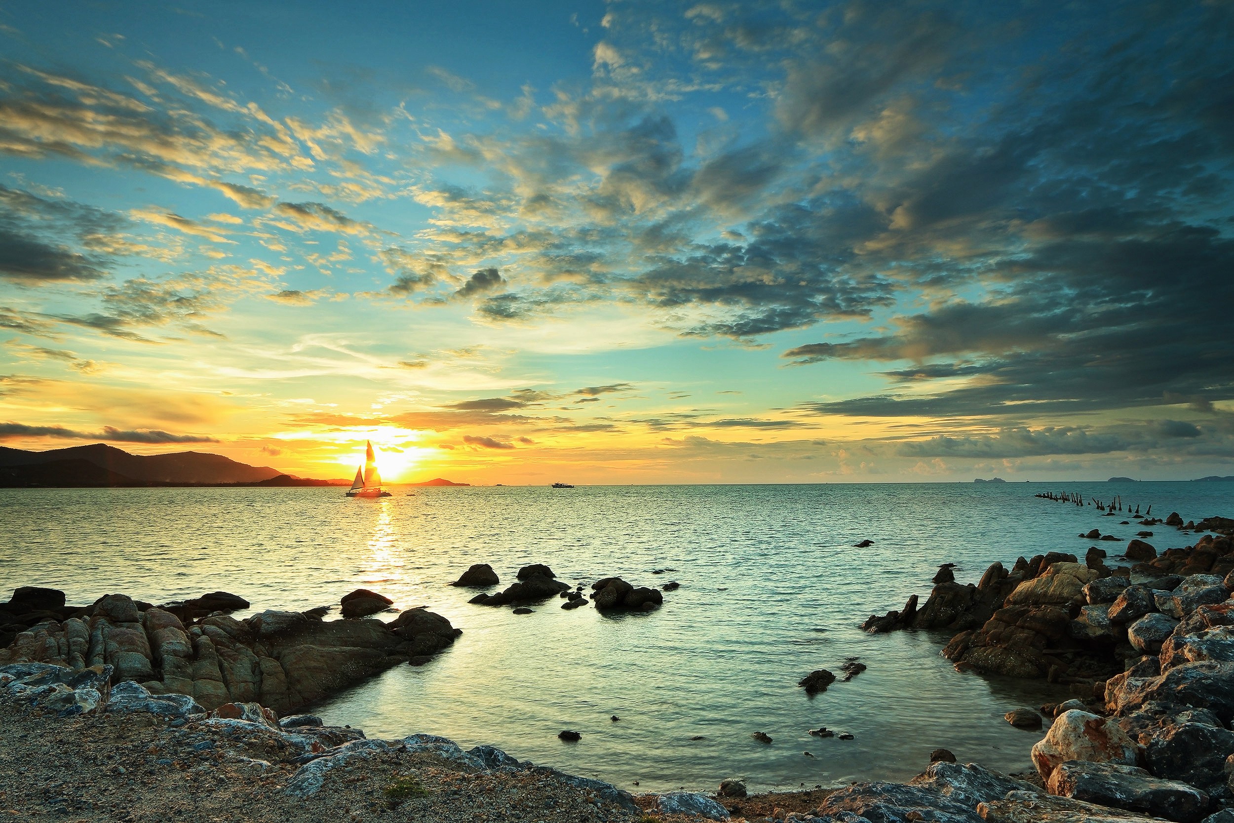 Sailboat on the ocean at sunset with rocky shore HD Wallpaper