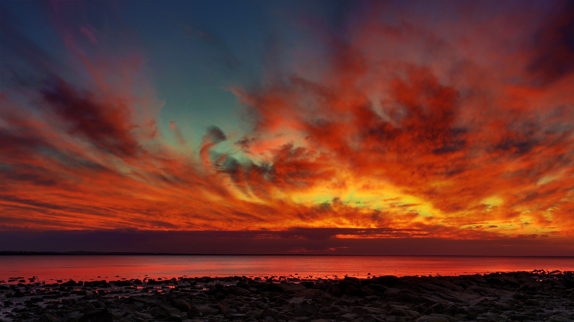 Dramatic sunset over a rocky shore and calm water HD Wallpaper