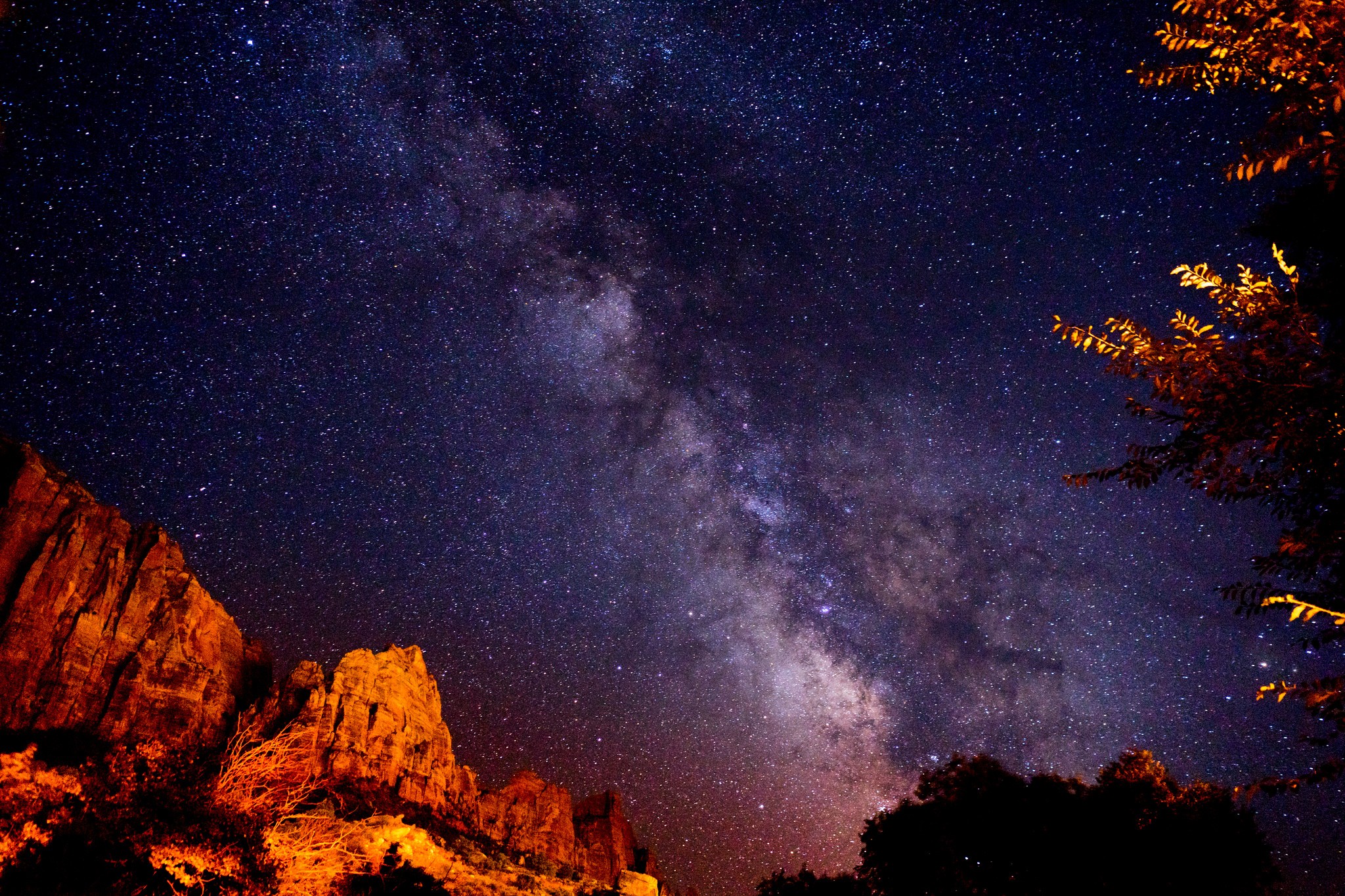 Milky Way over illuminated rock formations and trees HD Wallpaper