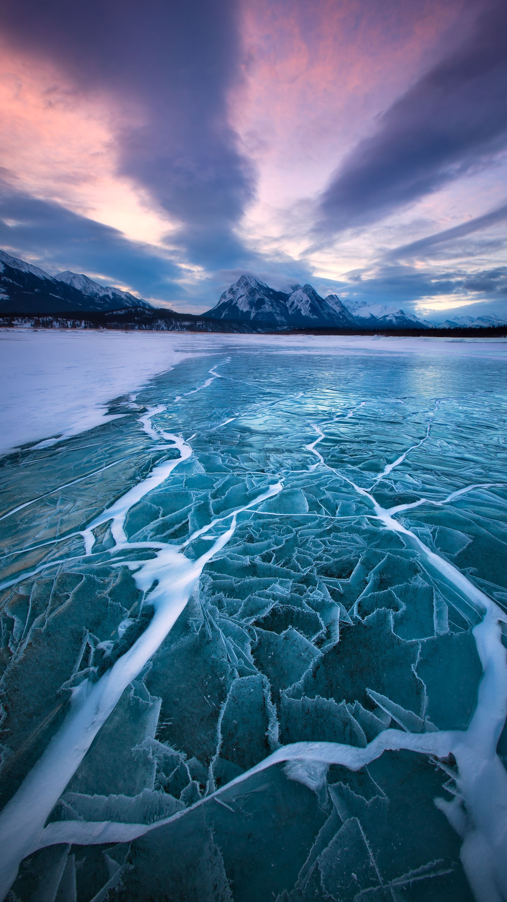 Cracked ice on a frozen lake with mountains and sunset sky HD Wallpaper