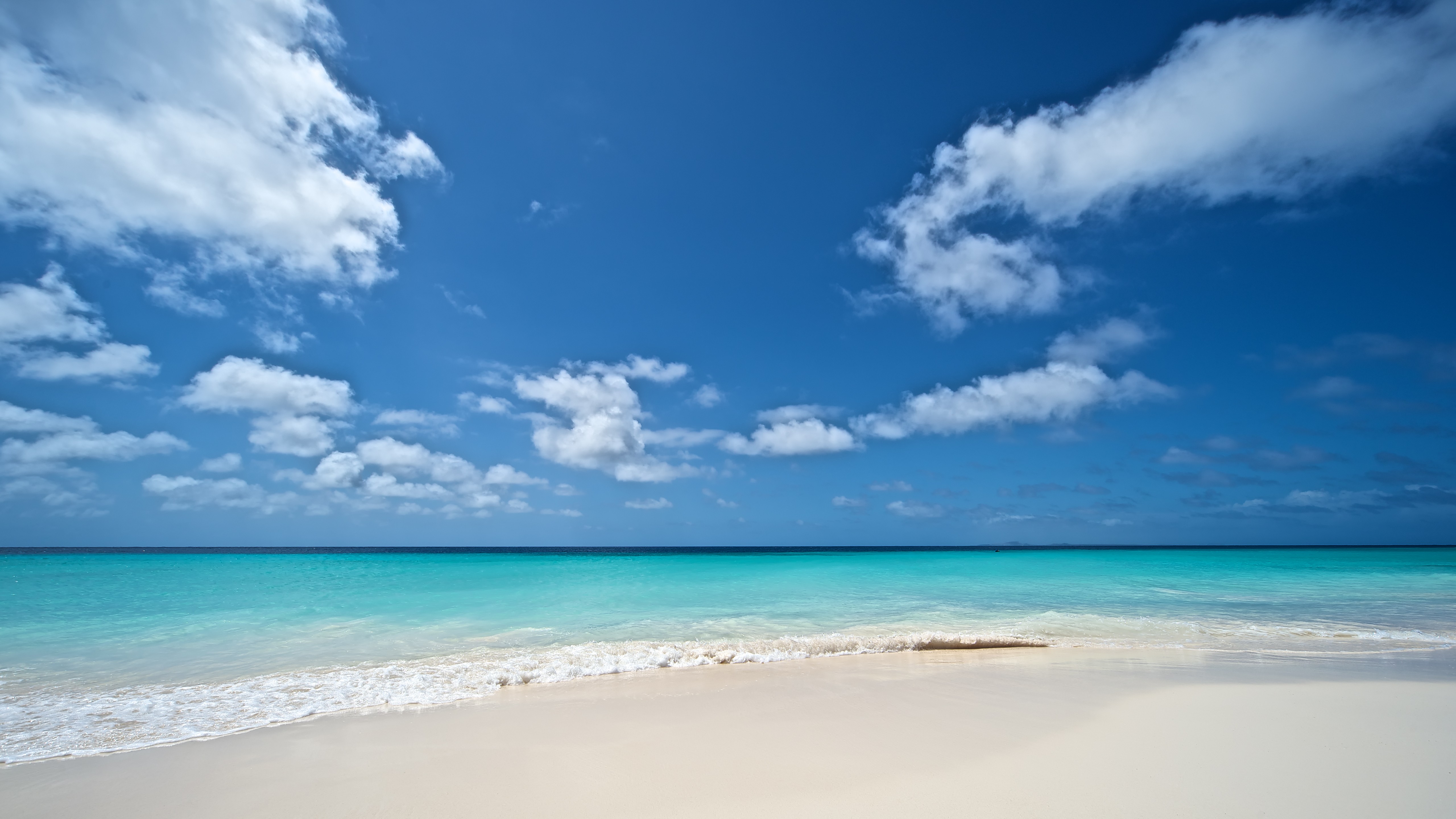 Turquoise ocean waves on a white sand beach under a blue sky with clouds HD Wallpaper