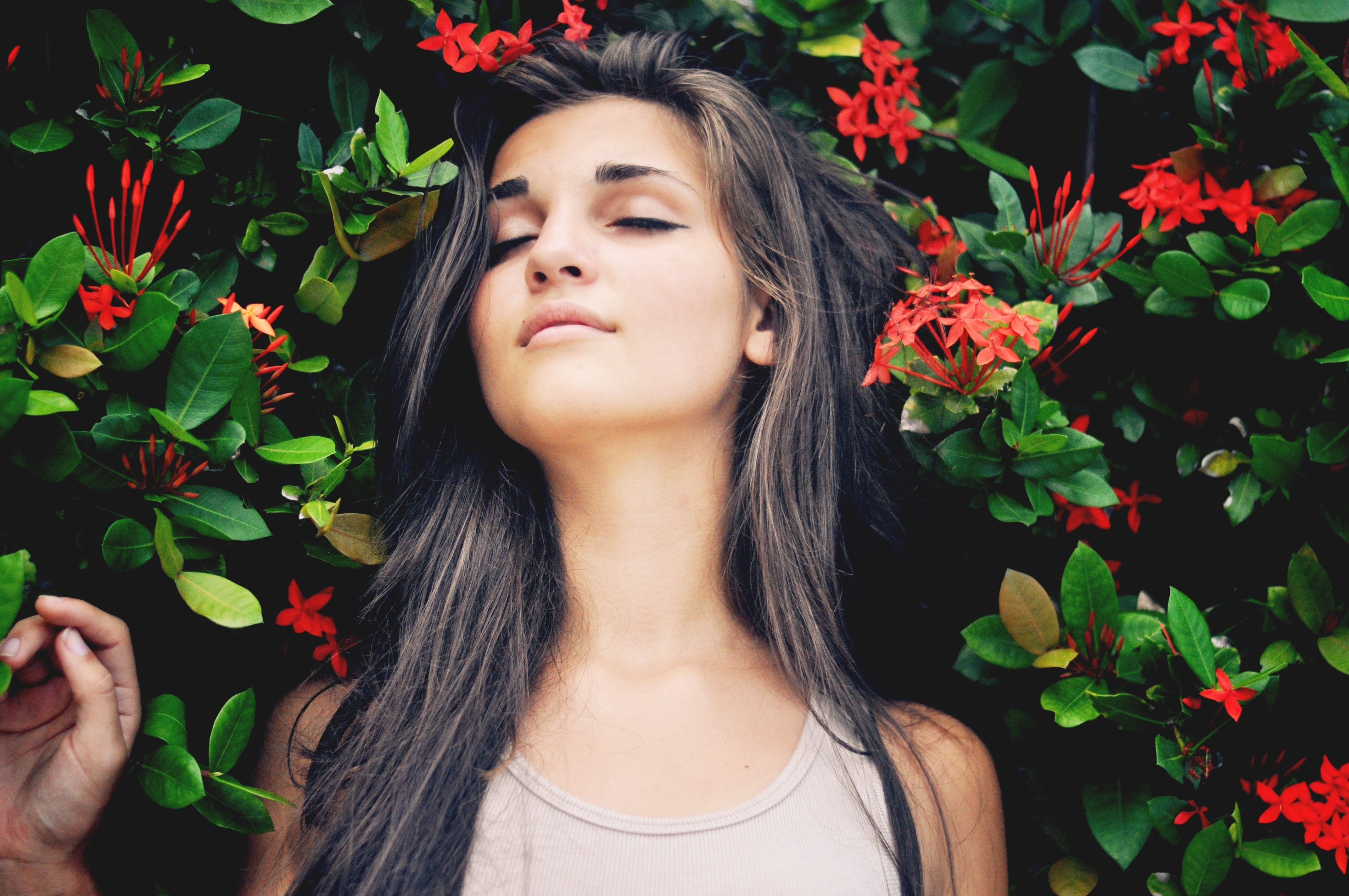 Woman with eyes closed among red flowers and green leaves HD Wallpaper