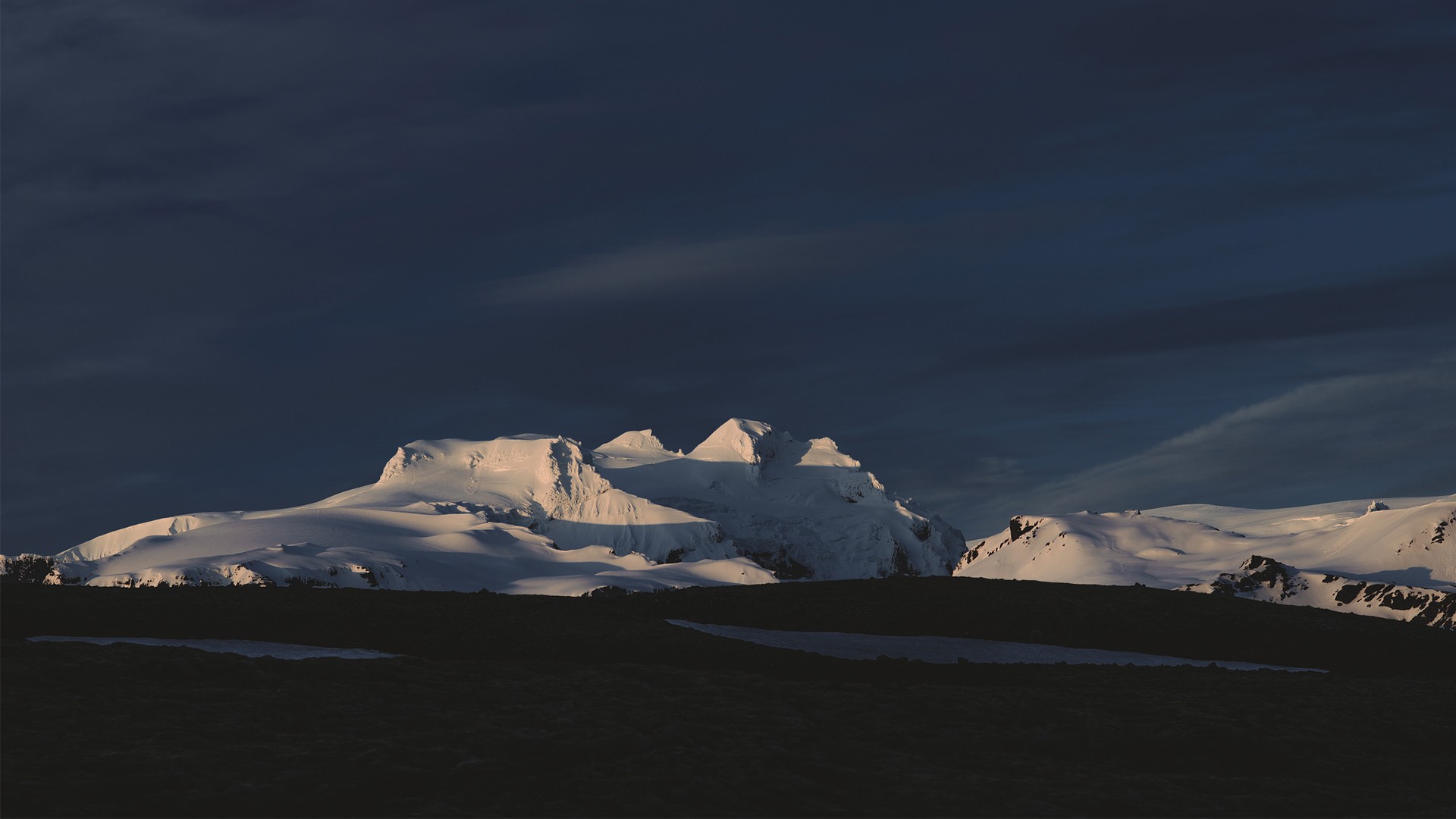 Snow-covered mountains under a dark sky HD Wallpaper
