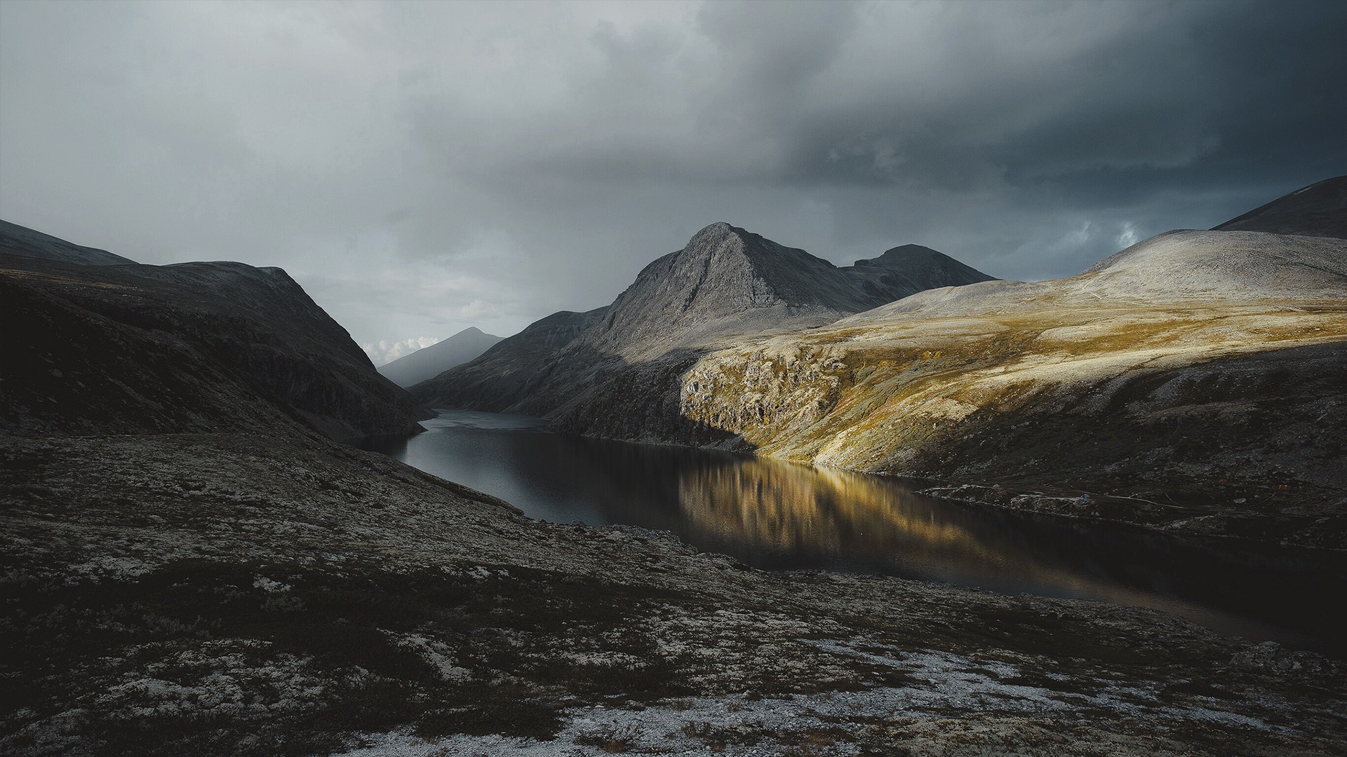 A dramatic mountain lake landscape under stormy skies HD Wallpaper