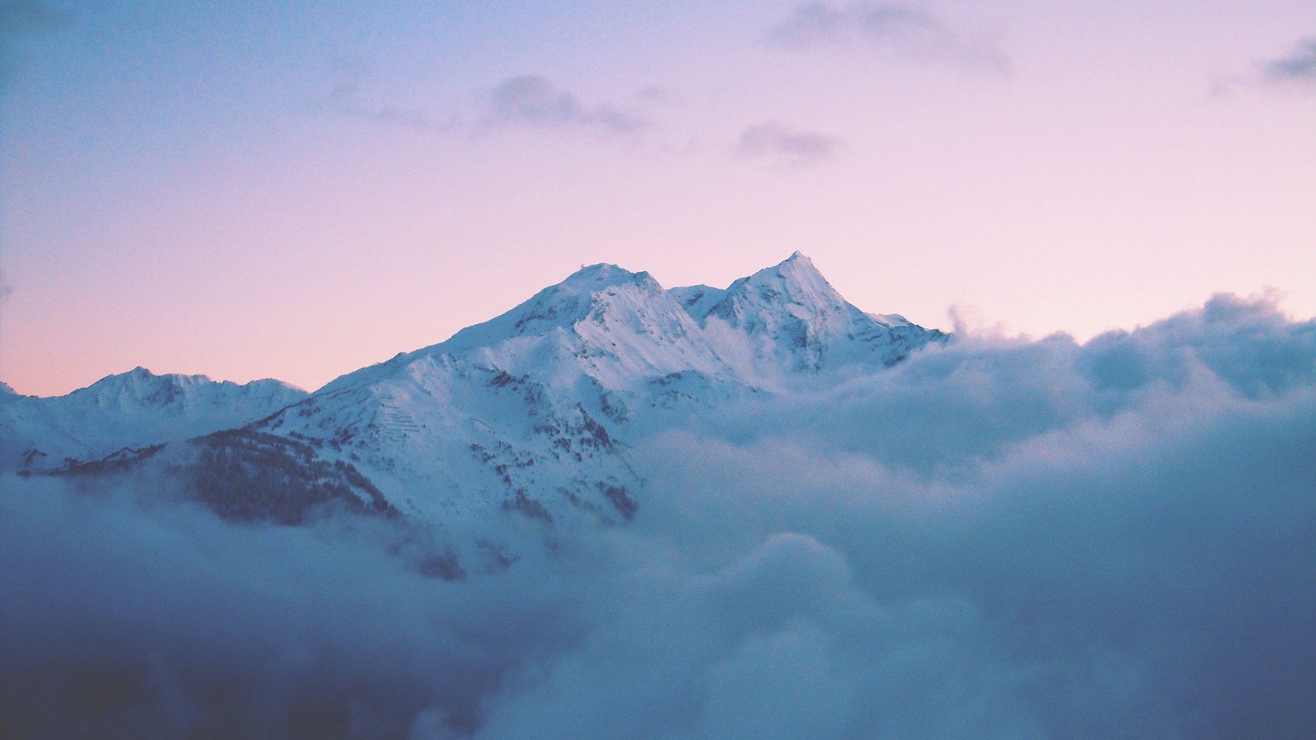 Snow-covered mountains emerge from clouds at sunset HD Wallpaper