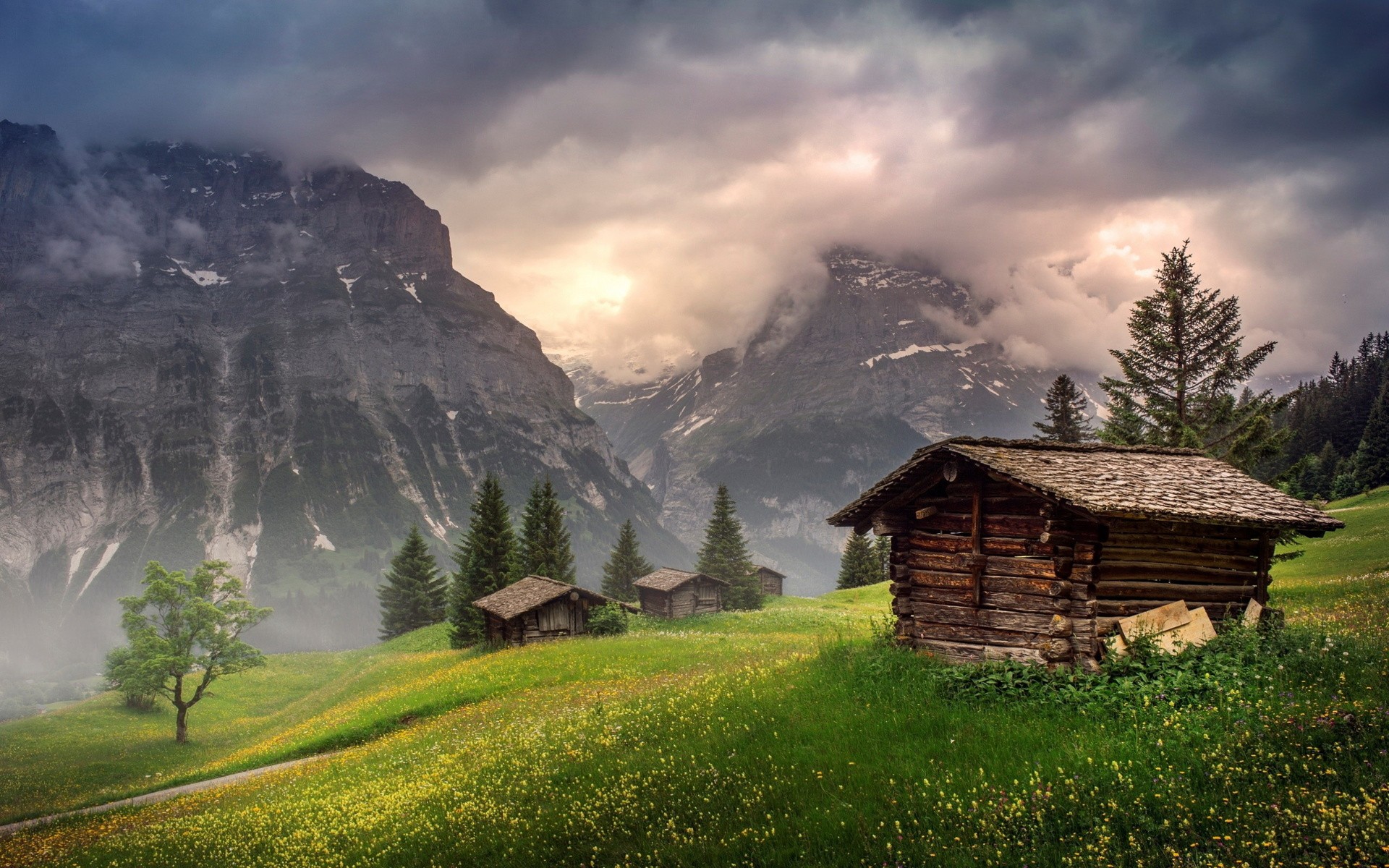 Wooden cabins in a green meadow with mountains HD Wallpaper