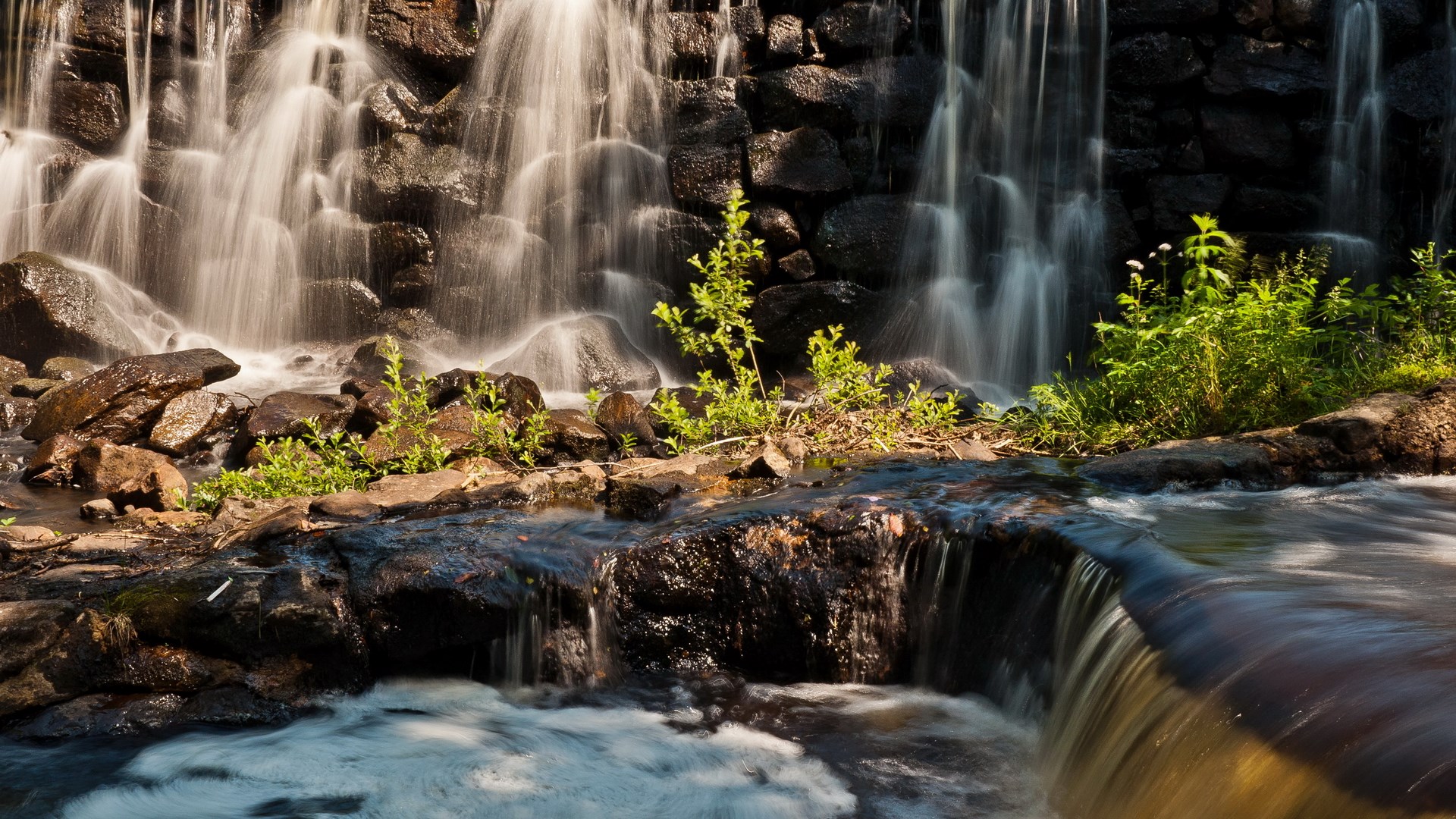 Waterfall cascading over rocks with green plants HD Wallpaper