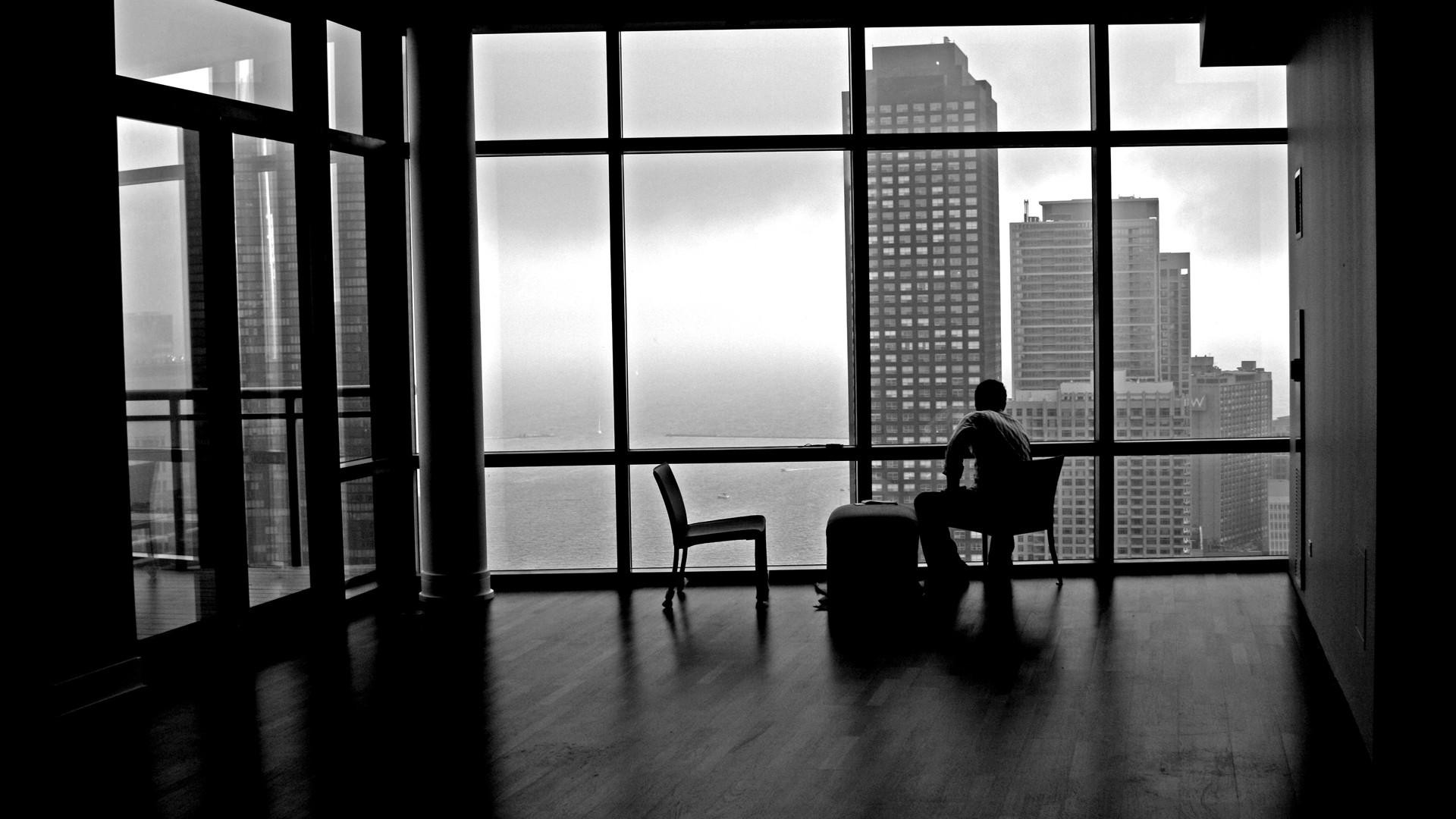 Man sitting in a modern apartment overlooking a city skyline HD Wallpaper