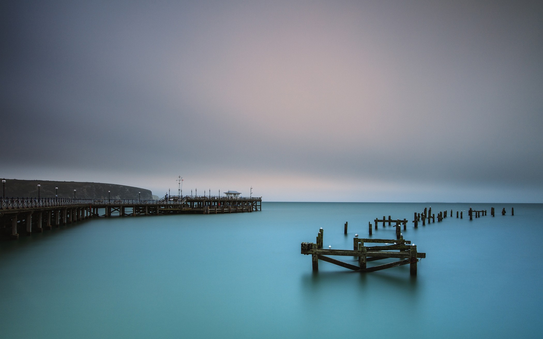 Old pier and wooden posts in the sea HD Wallpaper