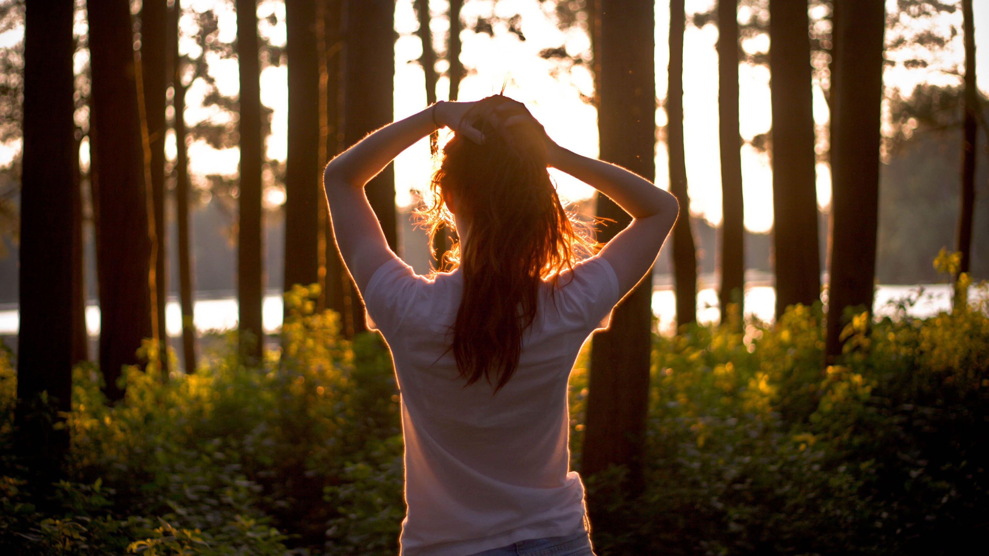Woman with hands in hair in forest at sunset HD Wallpaper