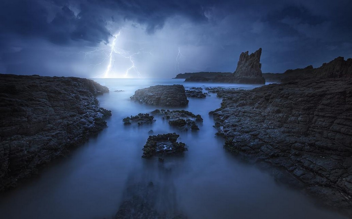 Lightning strikes over a rocky coast during a storm HD Wallpaper