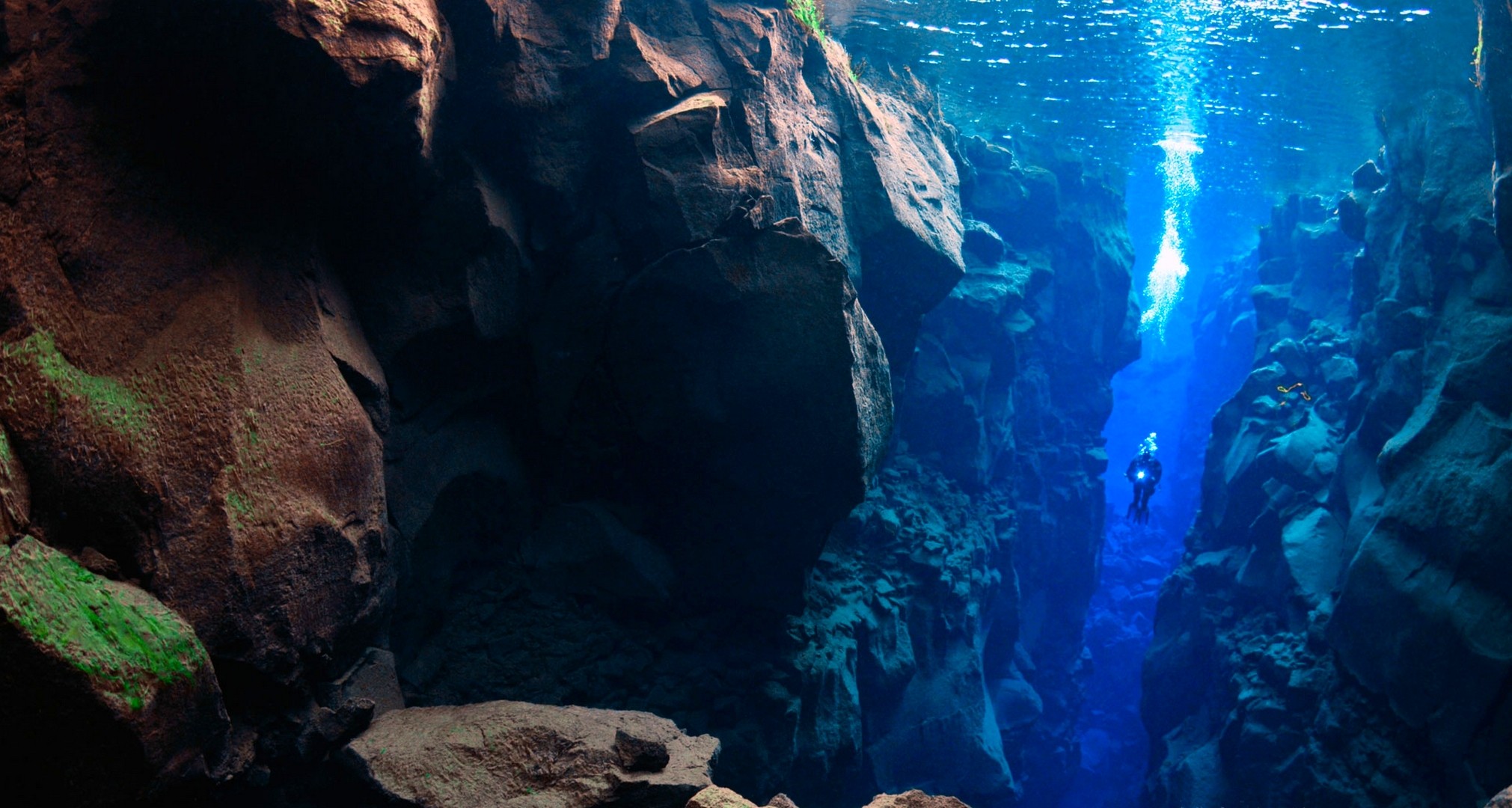 Scuba diver in a deep underwater rock crevice in Iceland HD Wallpaper