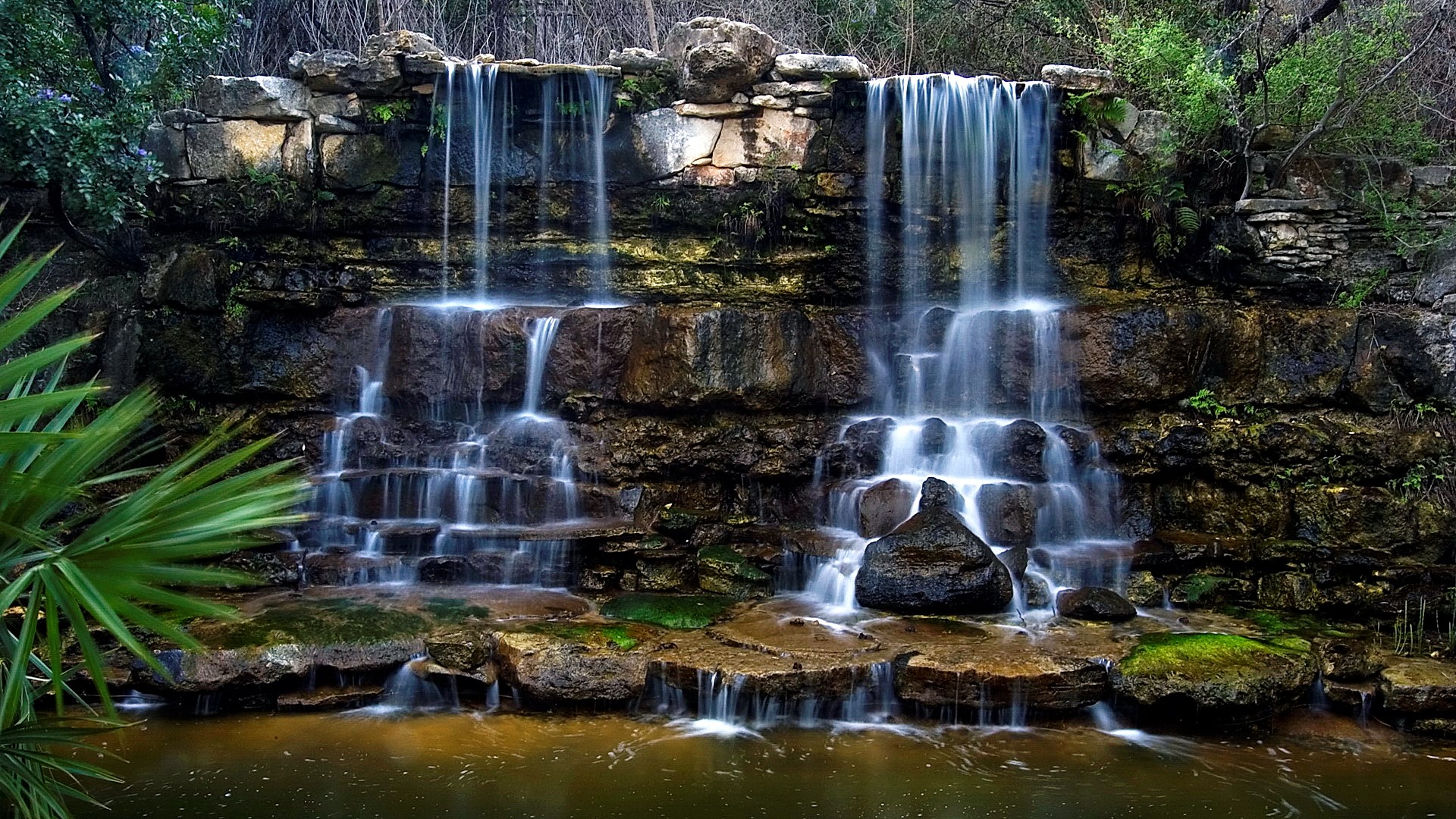 Multi-tiered waterfall cascading over rocks into a pool HD Wallpaper