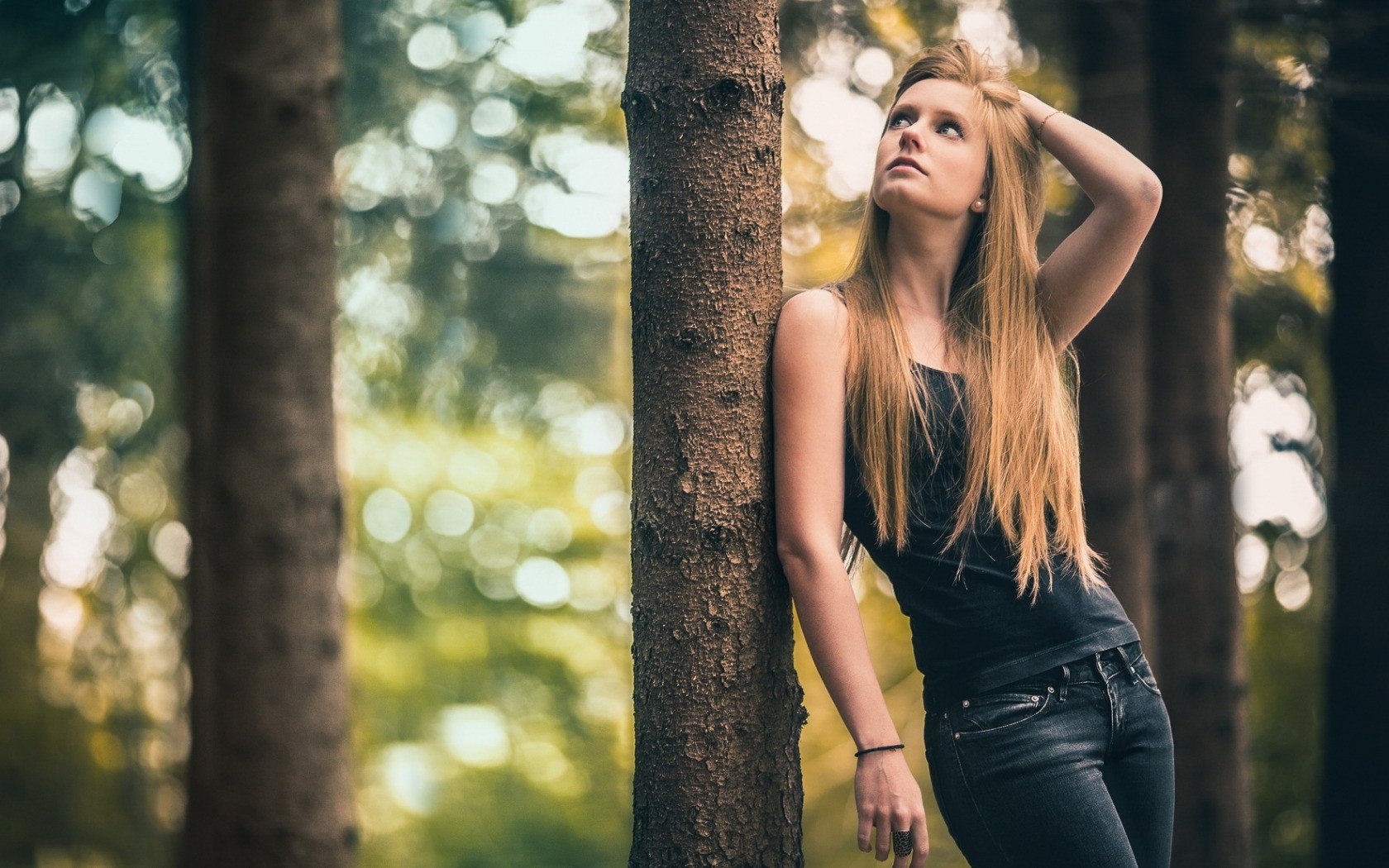 Woman with long blonde hair leaning against a tree in a forest HD Wallpaper