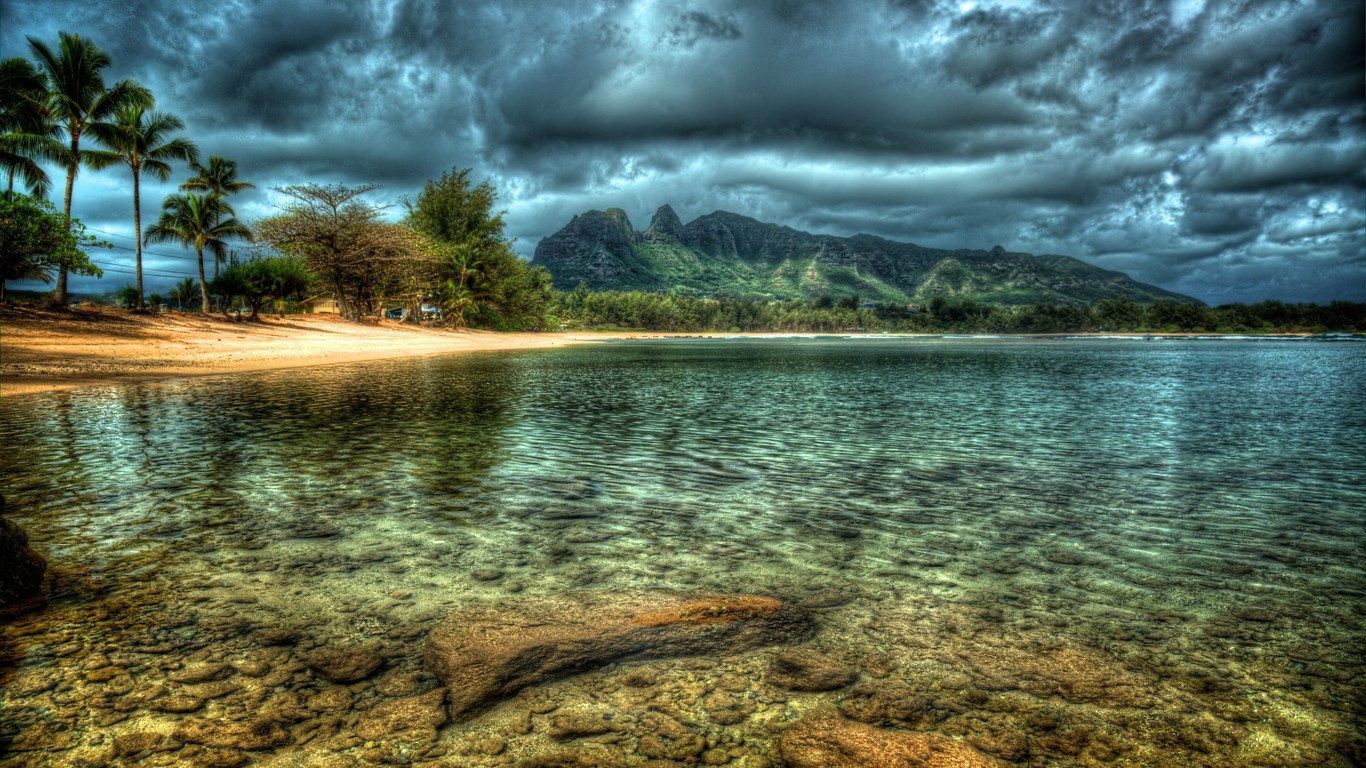 Beach with mountains and palm trees under stormy clouds HD Wallpaper