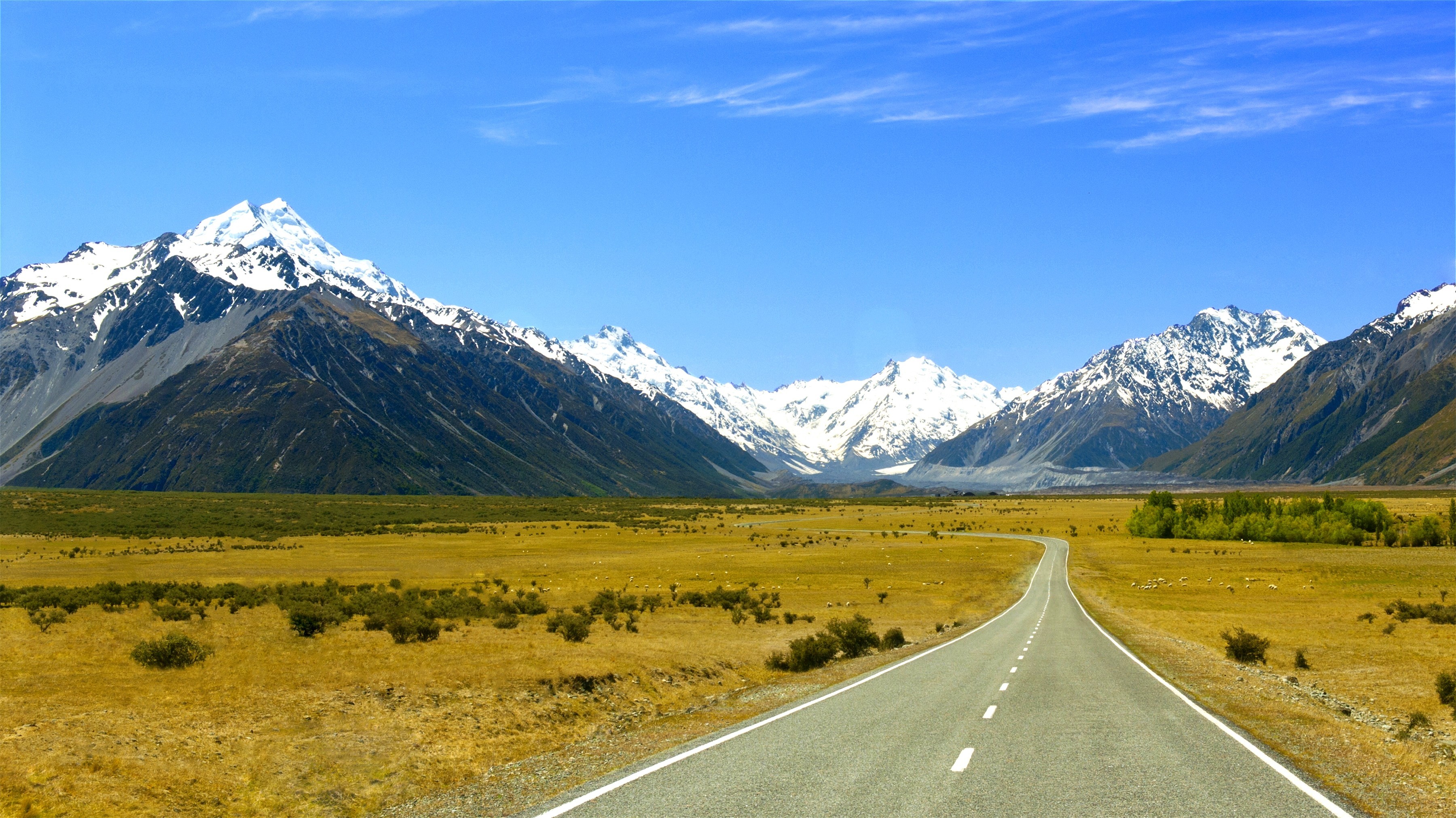 Road leading to snow-capped mountains under a blue sky HD Wallpaper